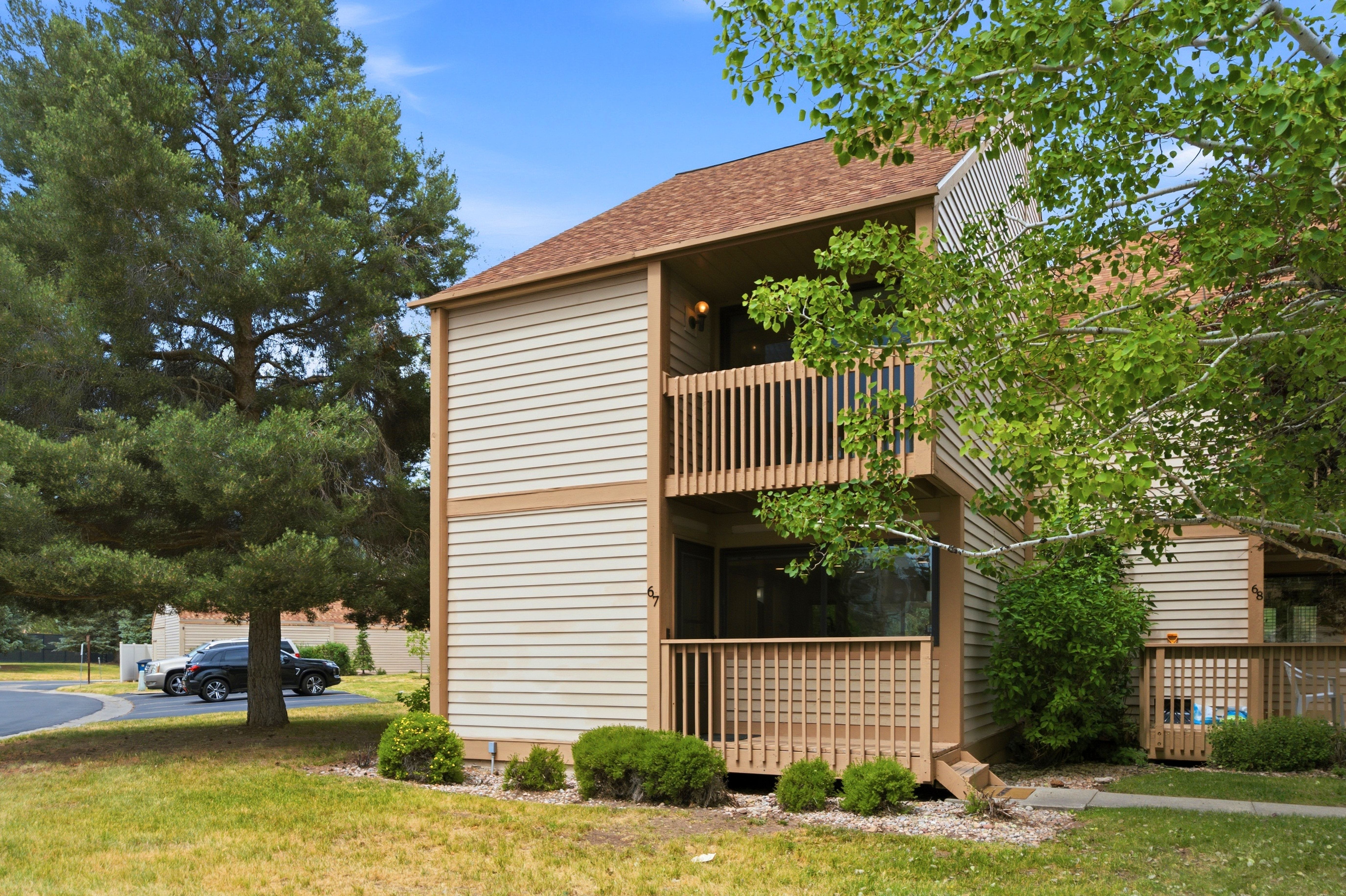 Two-story multi-unit structure featuring horizontal siding, a brown shingle roof, and a ground-level patio