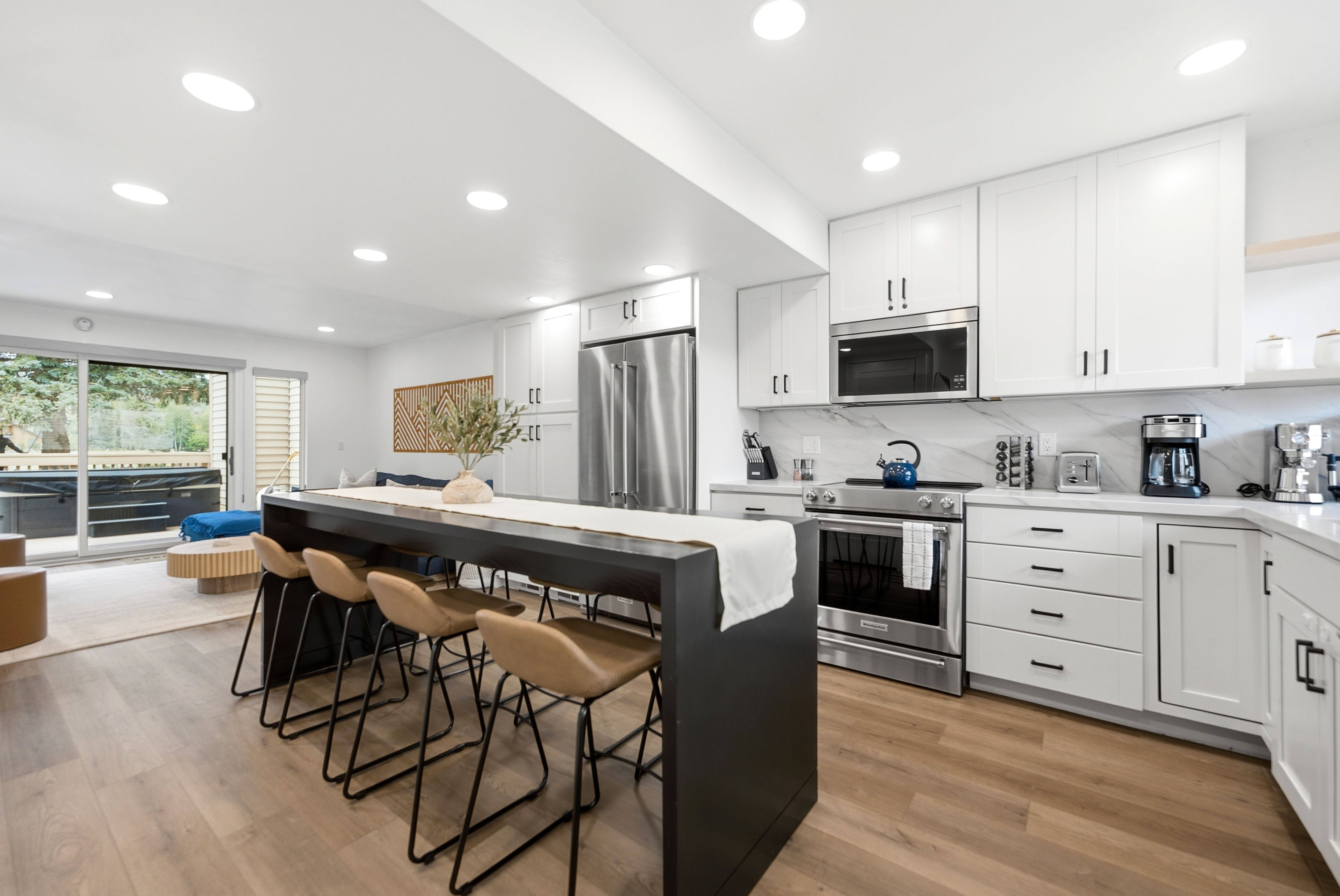 Open-concept living space featuring wood-finish flooring, recessed lighting, a sliding glass door, white upper and lower cabinetry, and stainless steel appliances