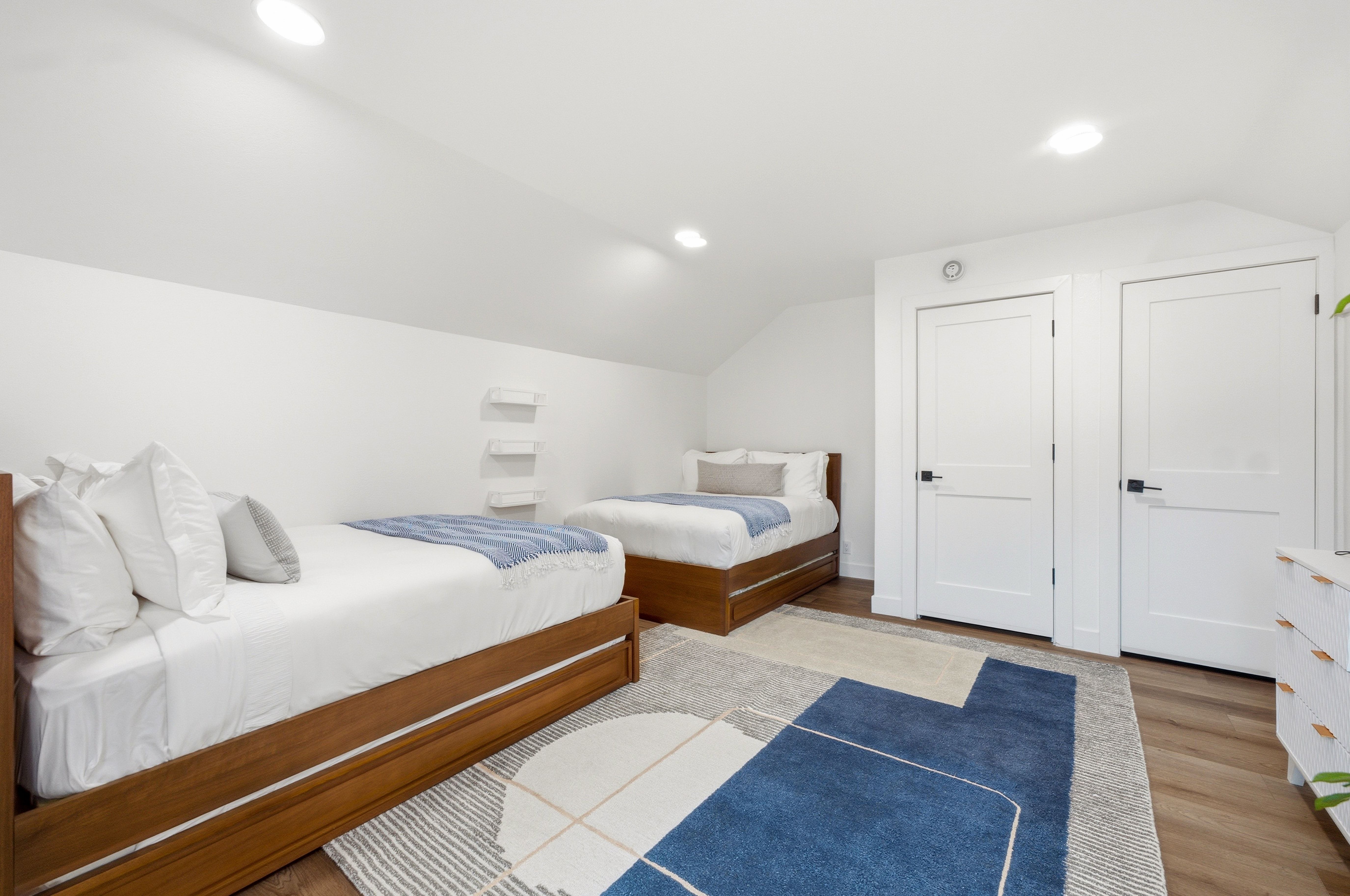 Spacious room featuring sloped ceilings, recessed lighting, wood-finish flooring, and white paneled doors with black hardware