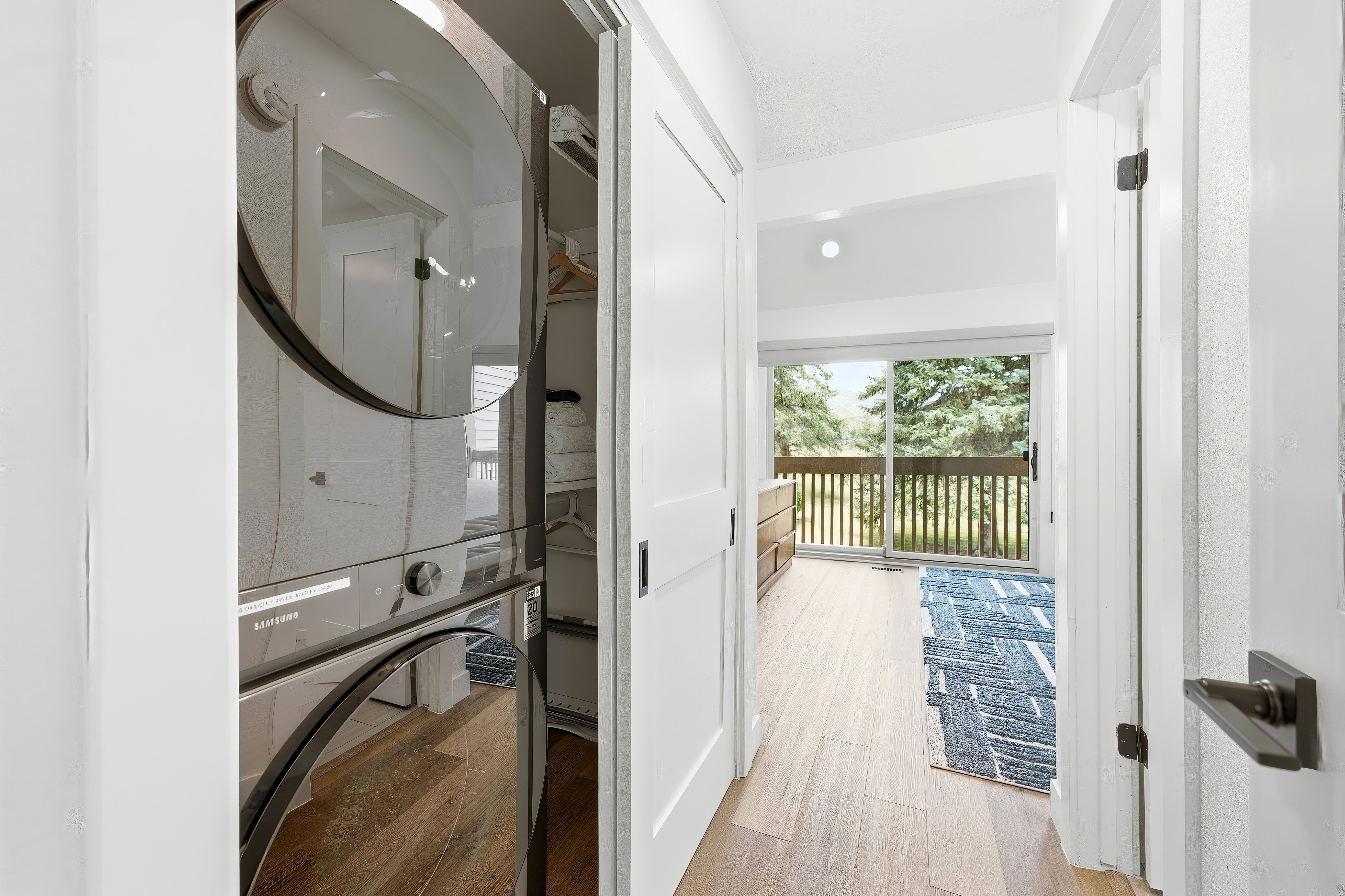 Stacked washer and dryer unit within a closet, featuring a white interior and wood-finish flooring