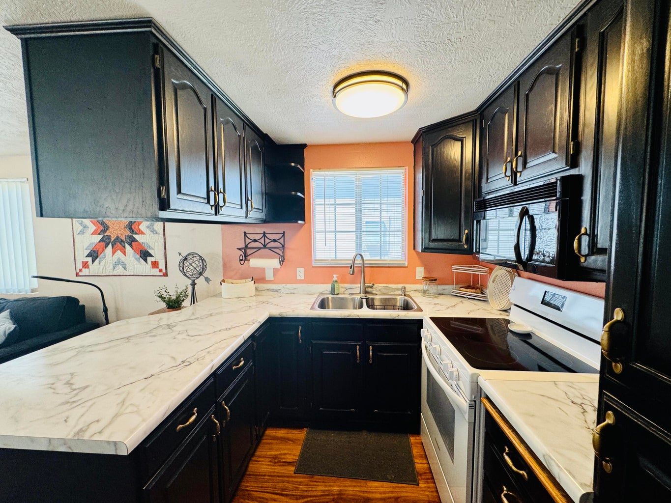 U-shaped kitchen featuring black cabinetry with brass hardware, wood-finish flooring, and white countertops with grey veining