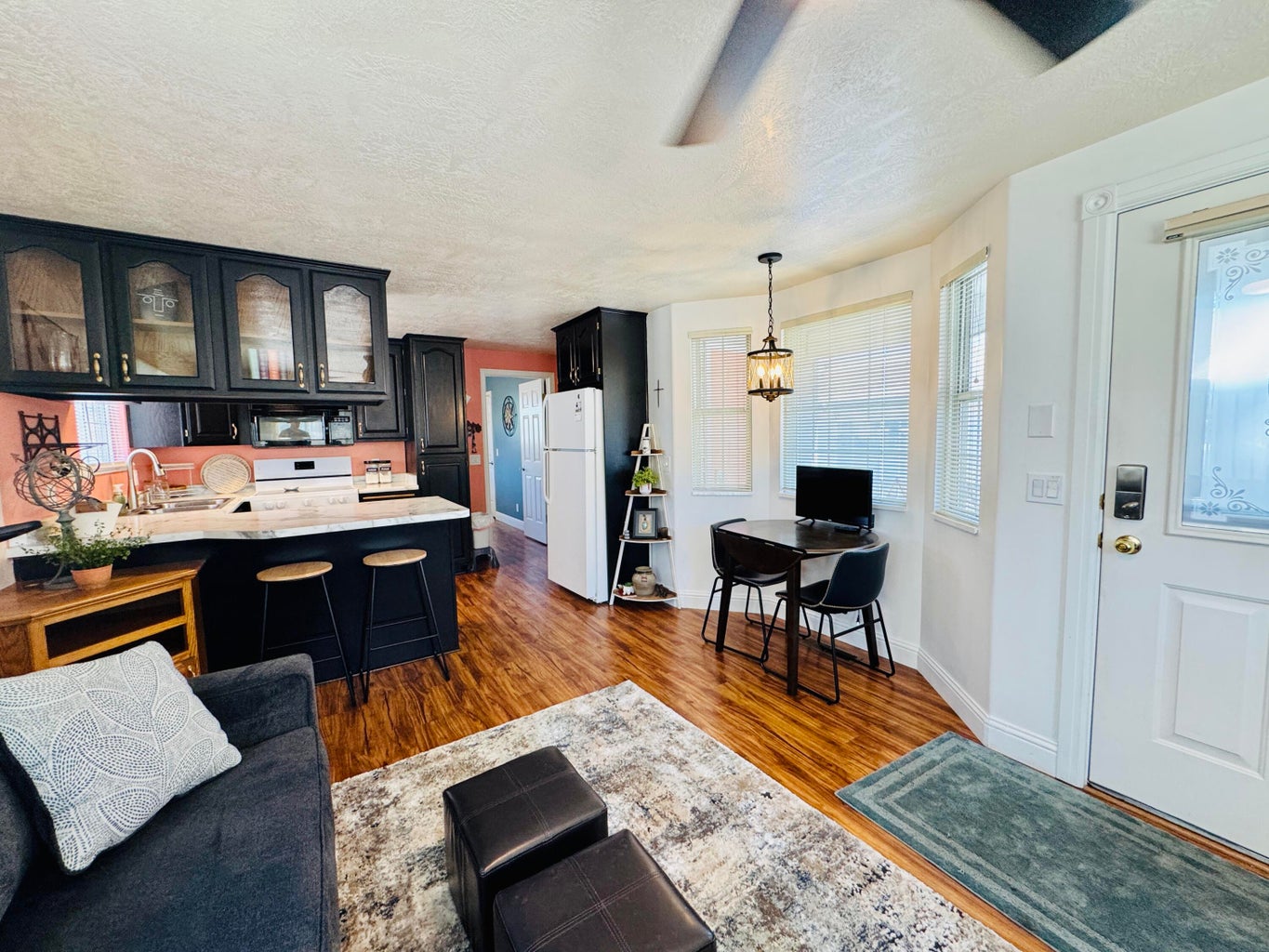 Open-concept living area featuring wood-finish flooring, a kitchen with dark cabinetry and light countertops, and a dining nook with bay windows