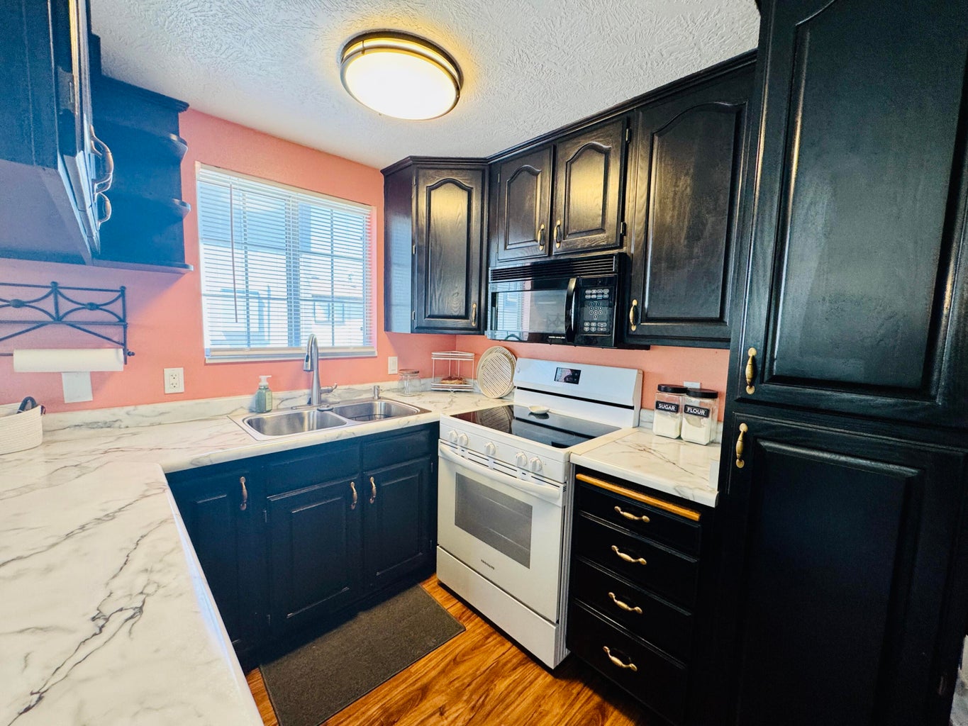 Kitchen featuring black cabinetry, white countertops with gray veining, a double basin stainless steel sink, a white electric range, and wood-finish flooring