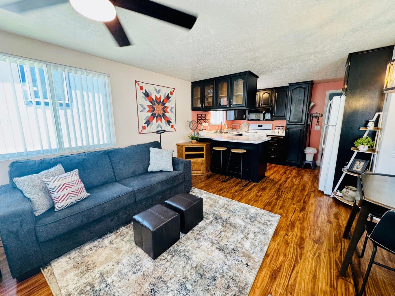 Open-concept living space featuring wood-finish flooring, a ceiling fan, and a kitchen with dark cabinetry, white countertops, and a built-in breakfast bar with seating