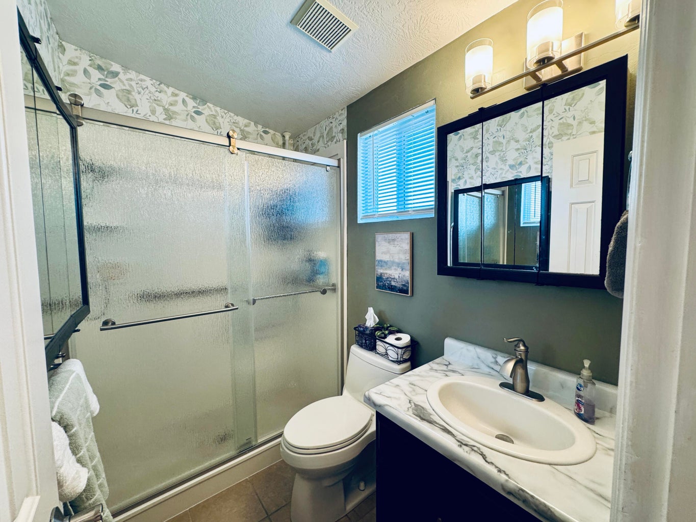 Bathroom featuring a shower with sliding textured glass doors, a vanity with a white countertop and integrated sink, and a wall-mounted medicine cabinet with mirrored doors