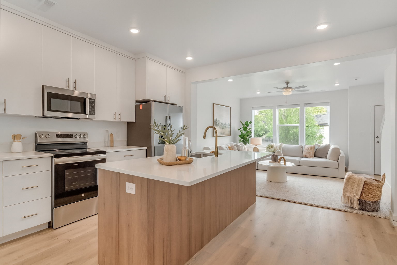 Open-concept kitchen featuring white cabinetry, stainless steel appliances, a central island with wood-finish paneling, and light wood-finish flooring