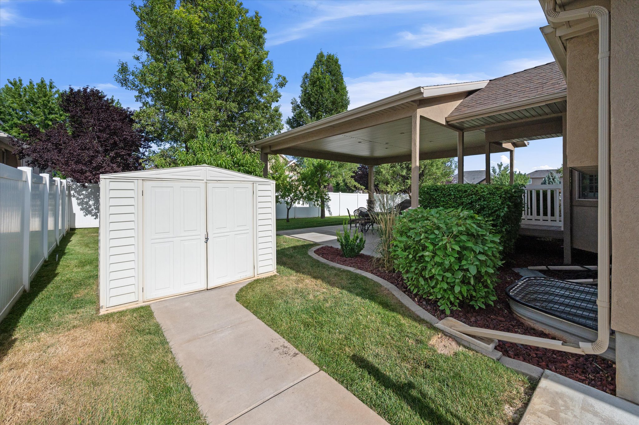 Expansive patio featuring a covered area with recessed lighting, concrete flooring, and surrounding shrubbery