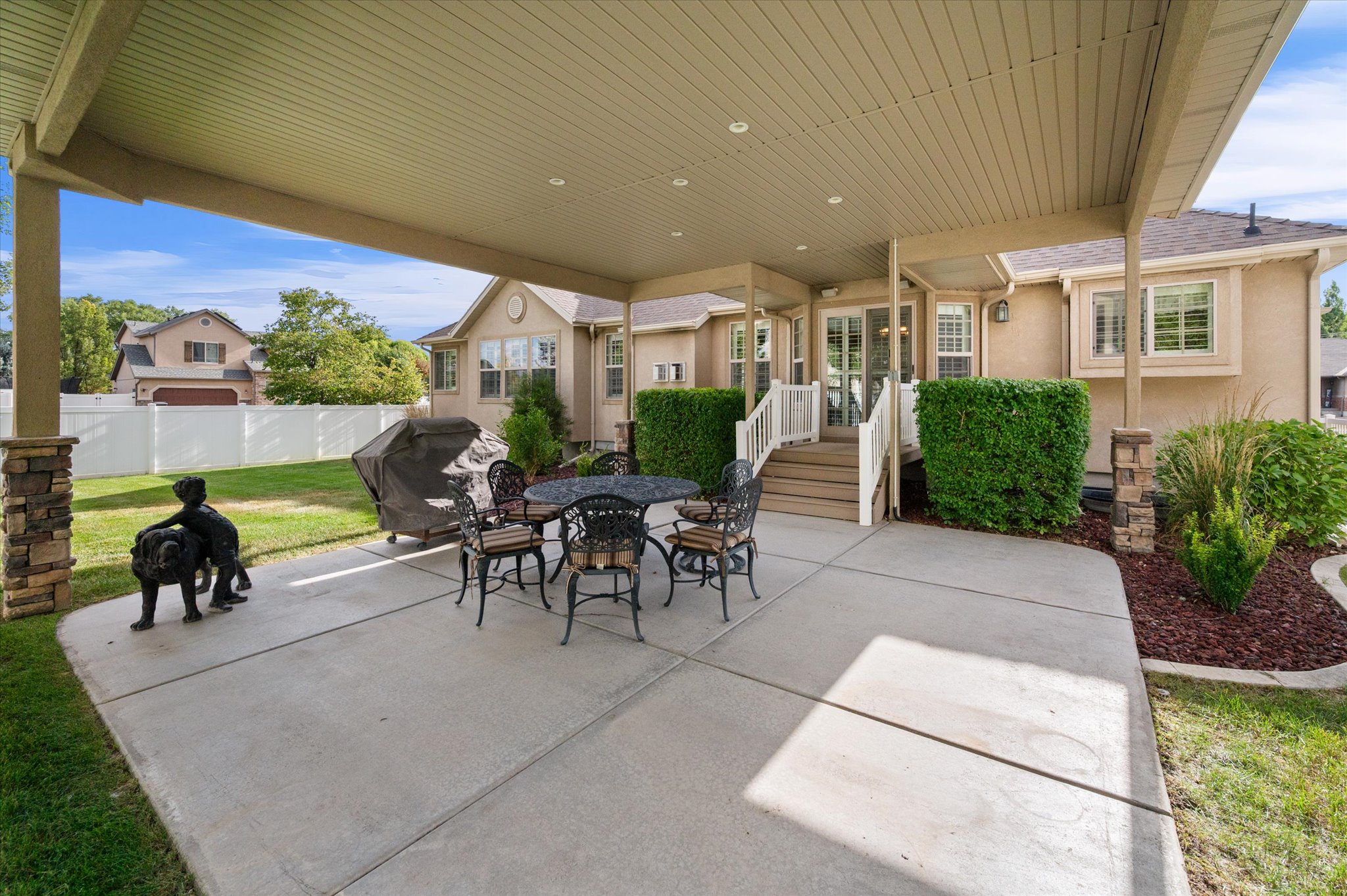 Expansive covered patio featuring a concrete slab, stone-clad support columns, and recessed lighting