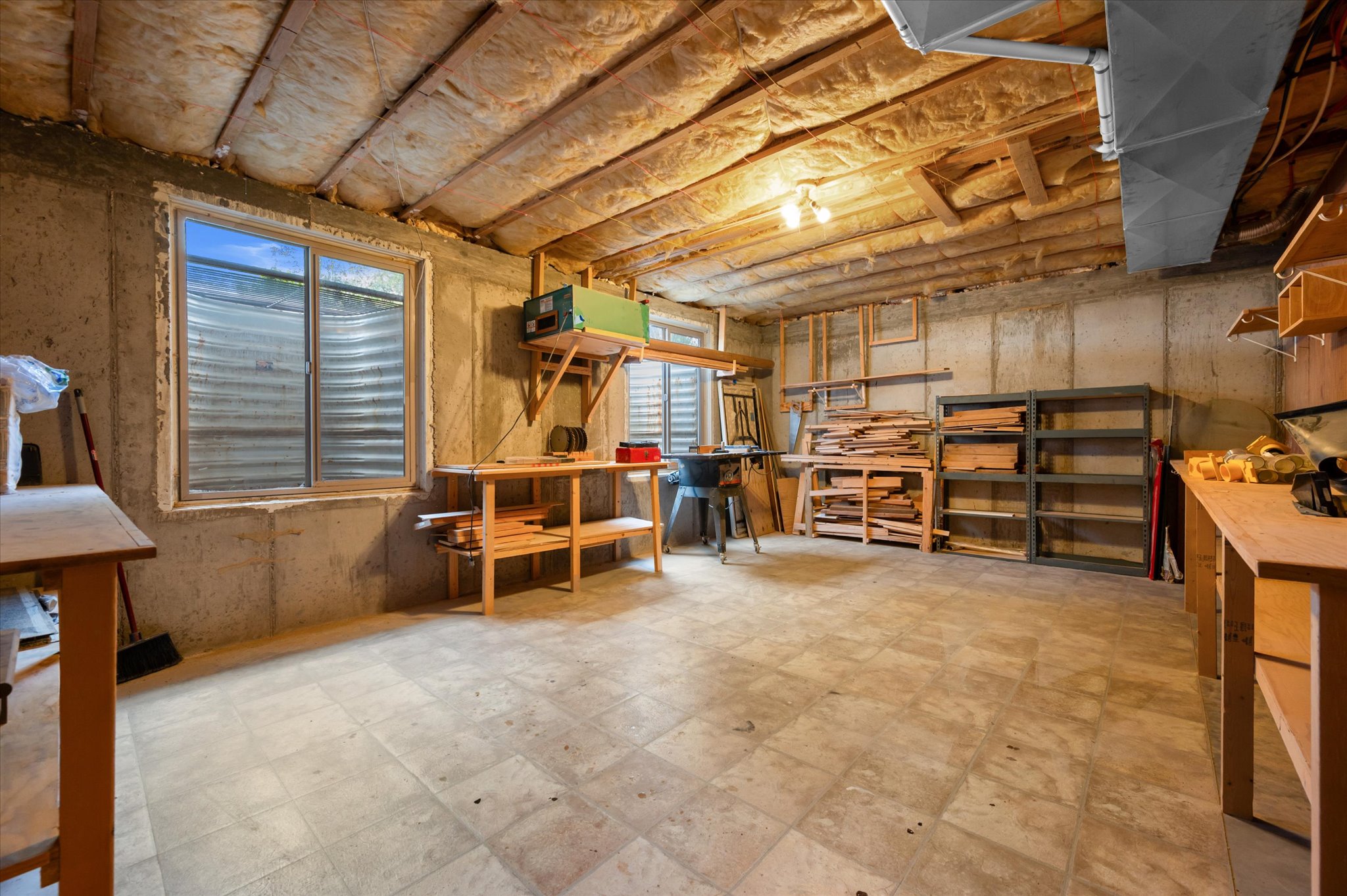 Finished basement space featuring exposed ceiling joists with insulation, concrete foundation walls, and light-toned tile flooring