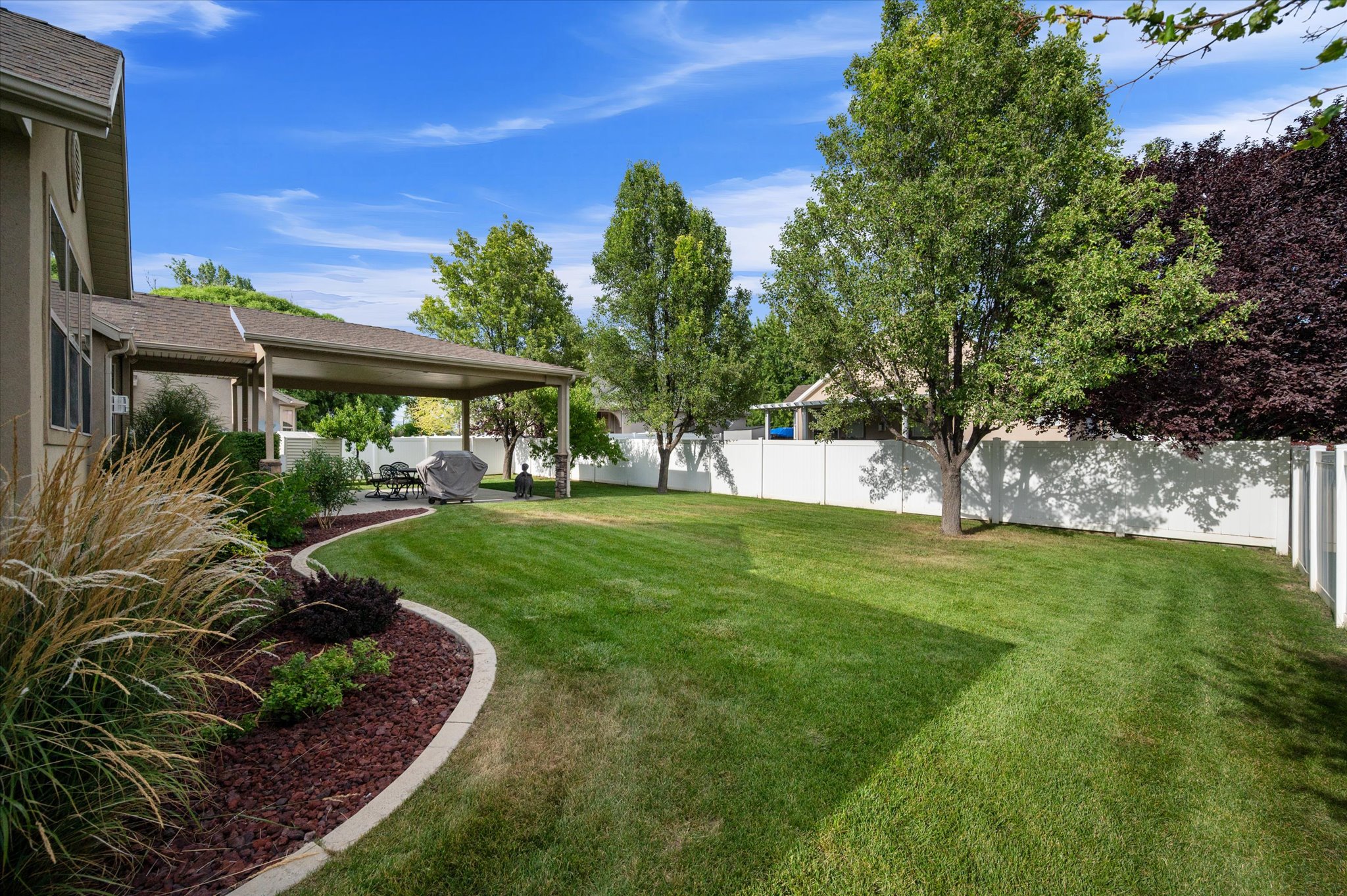 Expansive green lawn with mature trees and a covered patio area