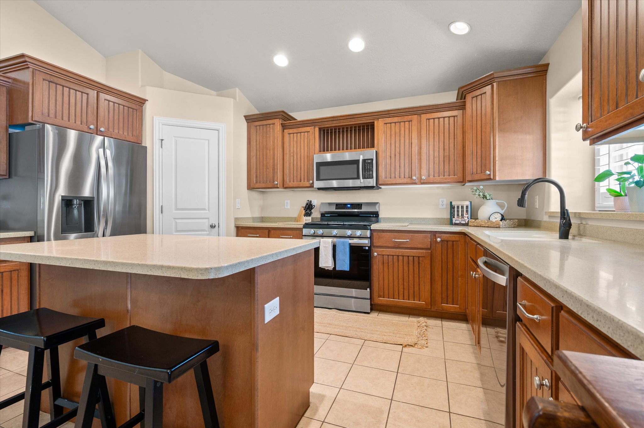Spacious kitchen featuring a central island with a light-toned countertop, extensive wood cabinetry, stainless steel appliances, and tile flooring