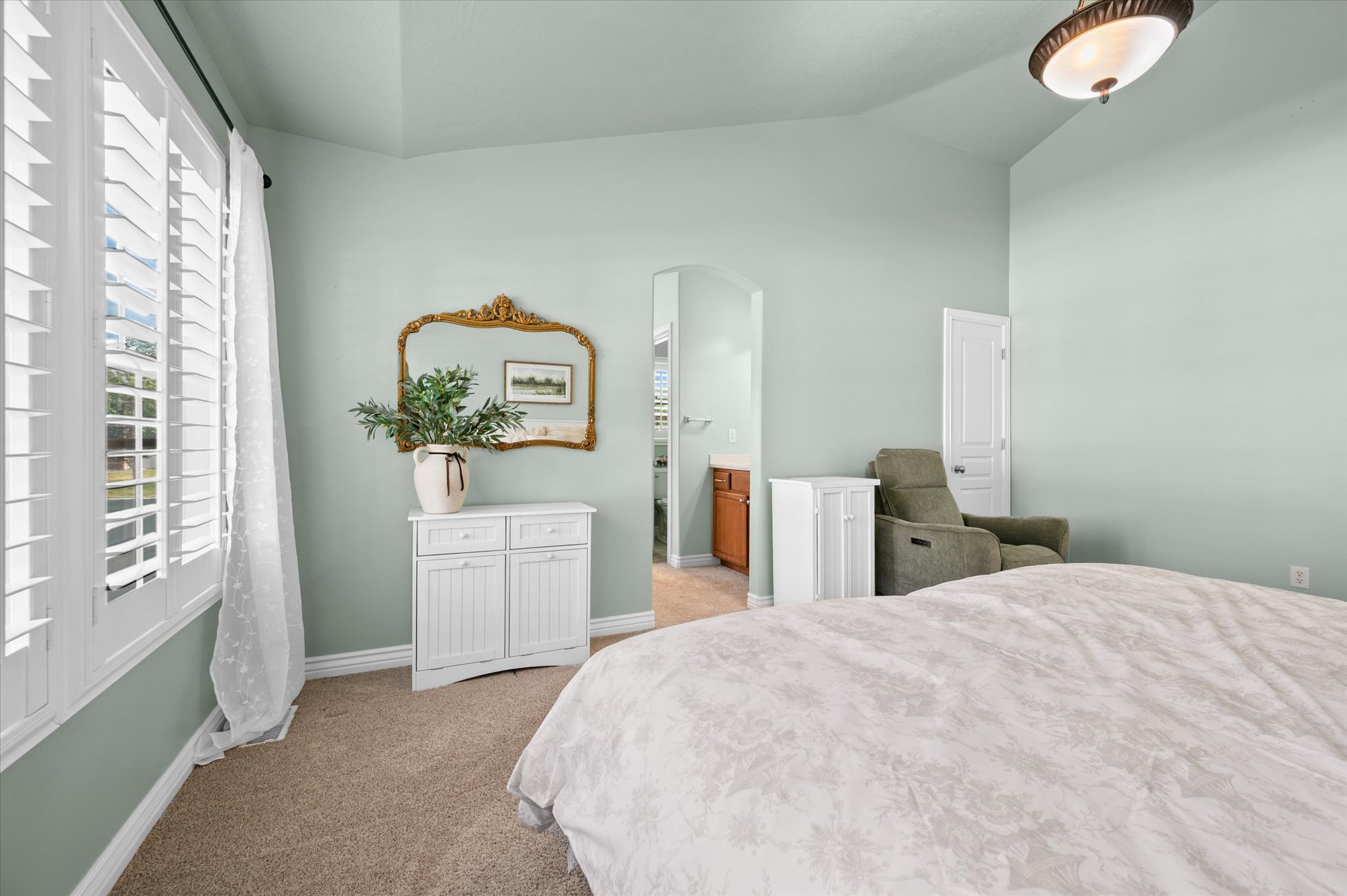 Carpeted room featuring a window with white plantation shutters, an arched doorway, and an overhead light fixture