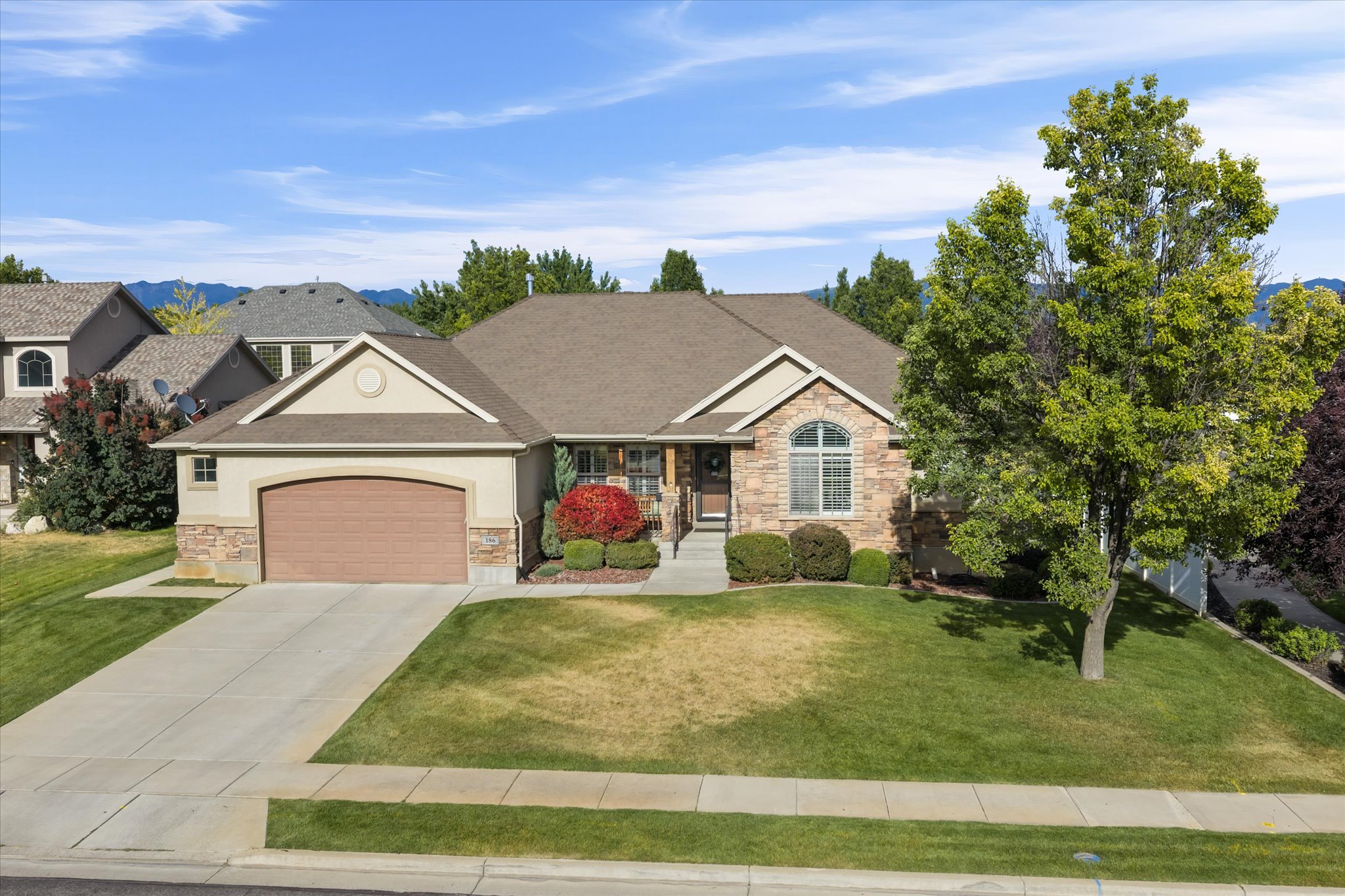 Single-story residence featuring a two-car garage, stone and stucco exterior, arched window with grilles, and mature landscaping