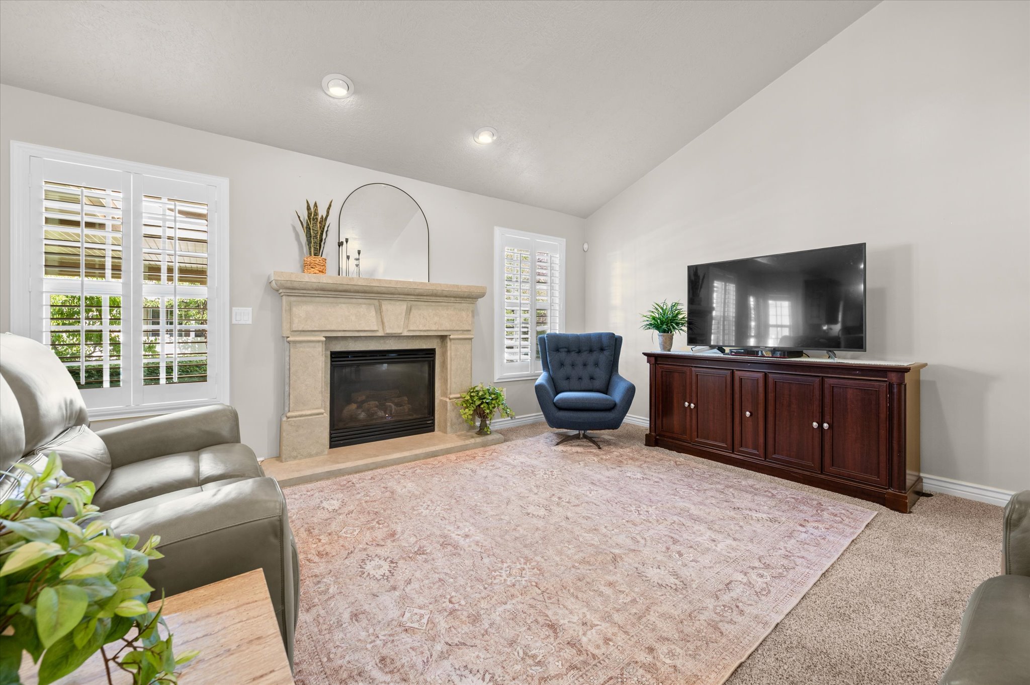 Living room featuring a stone-clad fireplace, vaulted ceiling, recessed lighting, and plantation shutters on the windows
