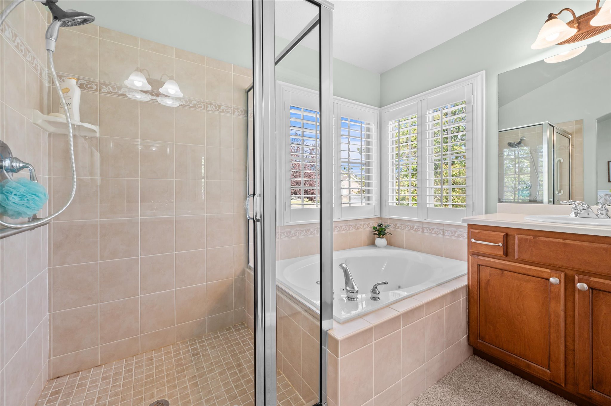 Bathroom featuring a glass-enclosed shower with tile surround, a corner soaking tub with plantation shutters, and a wood vanity with a white countertop
