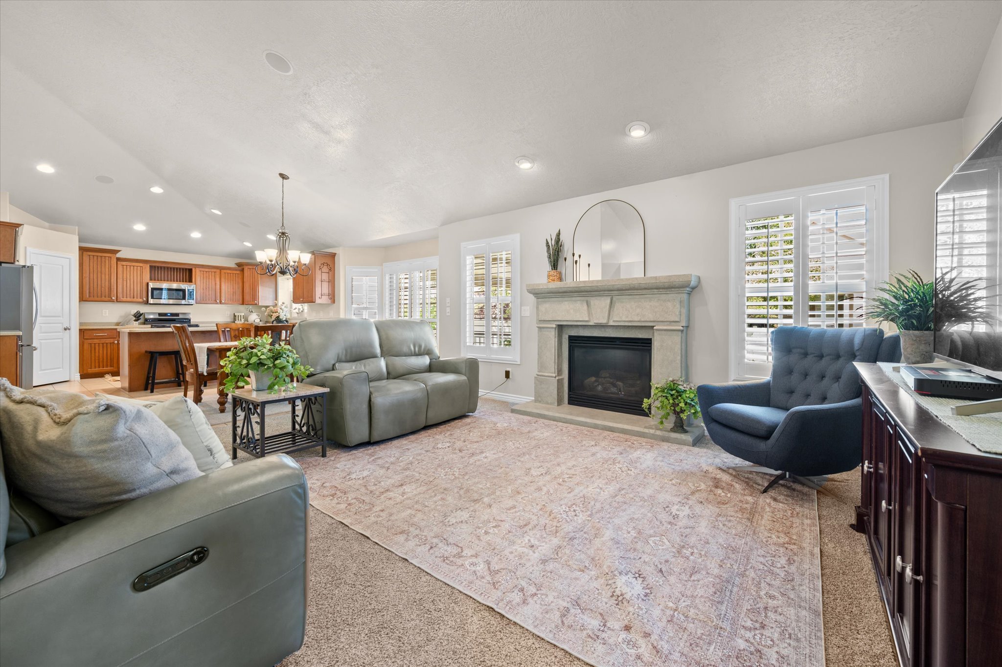 Open concept living area featuring a built-in fireplace with a stone surround, recessed lighting, and plantation shutters