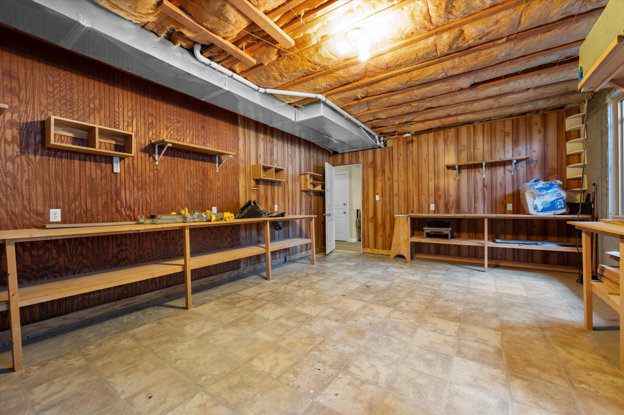 Spacious unfinished basement featuring wood paneling, exposed ceiling joists, and built-in shelving and workbenches