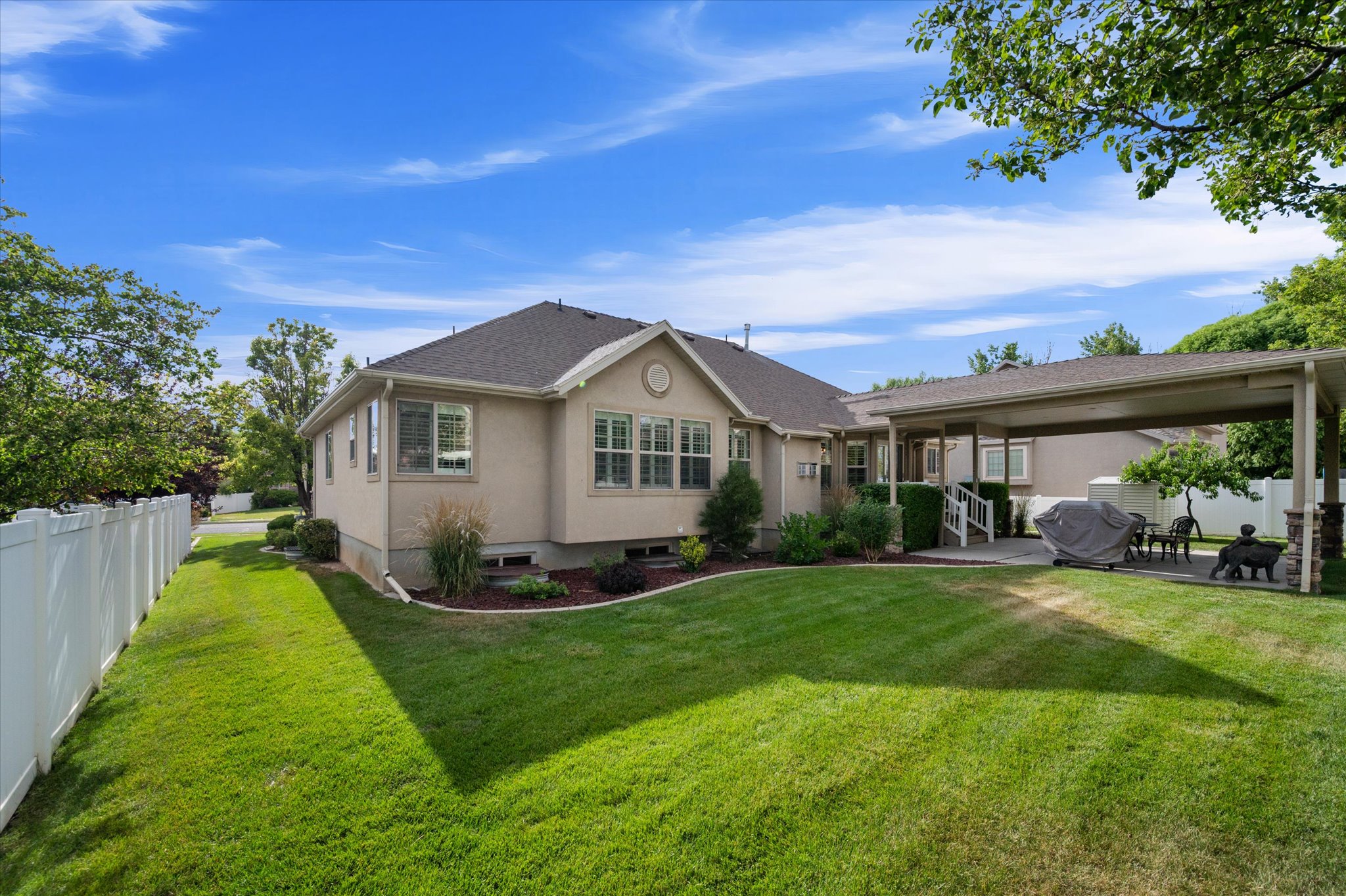 Spacious rear yard featuring an expansive lawn, mature trees, and a white privacy fence