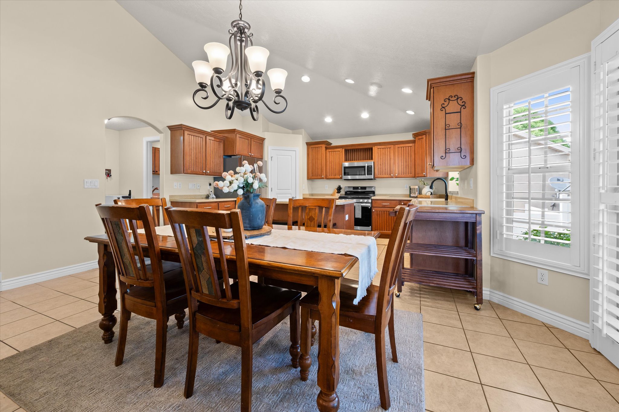 Vaulted ceiling dining area featuring a decorative chandelier, tile flooring, and plantation shutters
