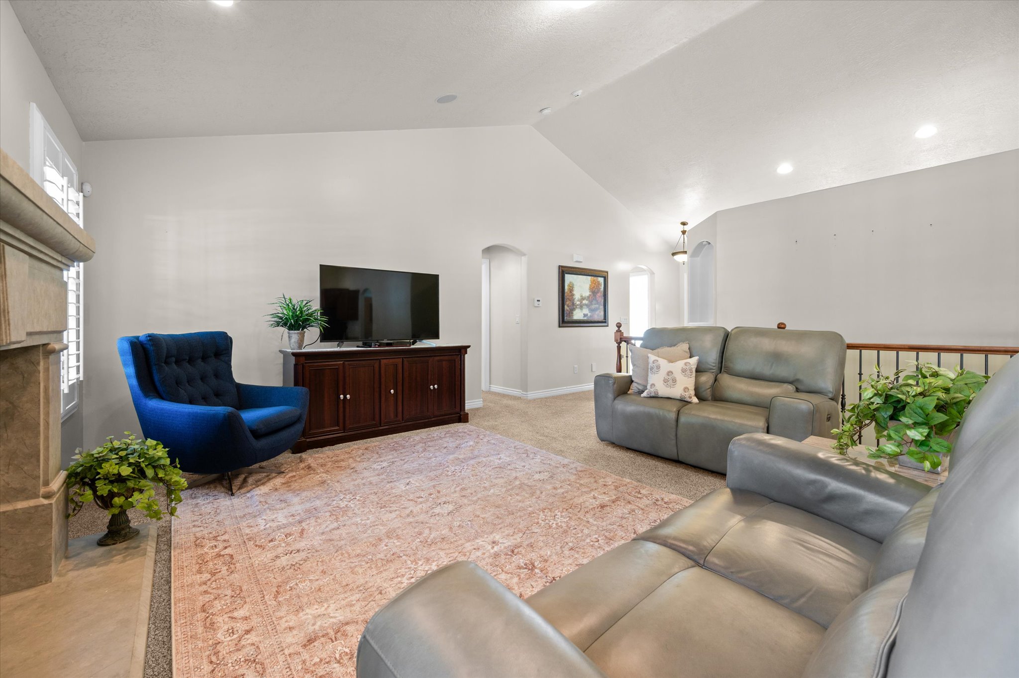 Spacious living area featuring vaulted ceilings, recessed lighting, a stone-clad fireplace, and a wood media console