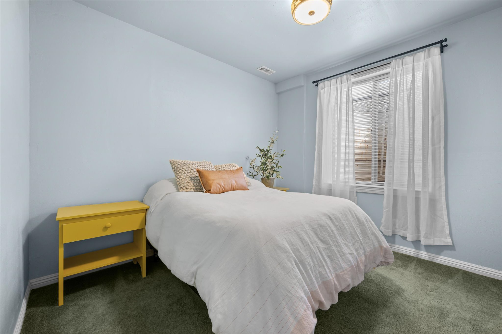 Bedroom featuring light blue walls, green carpet flooring, and a single window with blinds