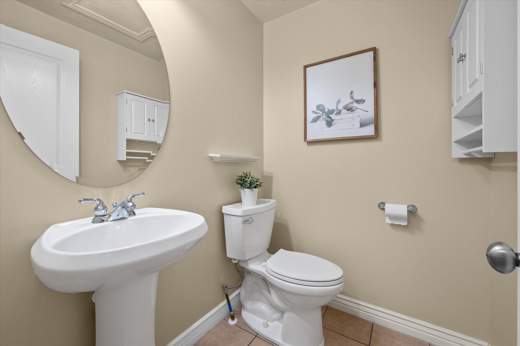 Pedestal sink with chrome faucet, oval wall mirror, and neutral wall paint