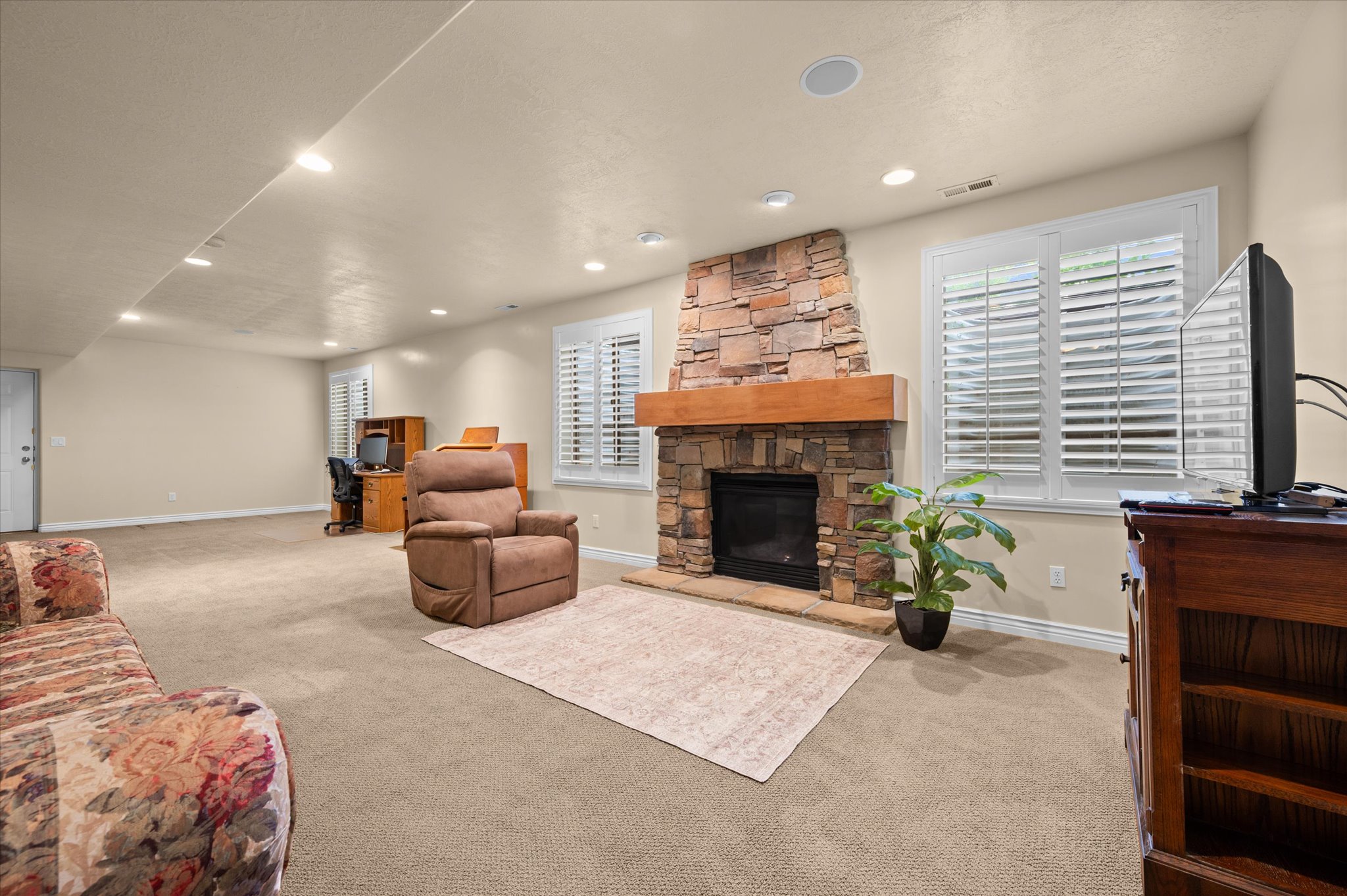 Spacious room featuring a stone-clad fireplace with a wood mantel, recessed lighting, and light-colored carpet flooring