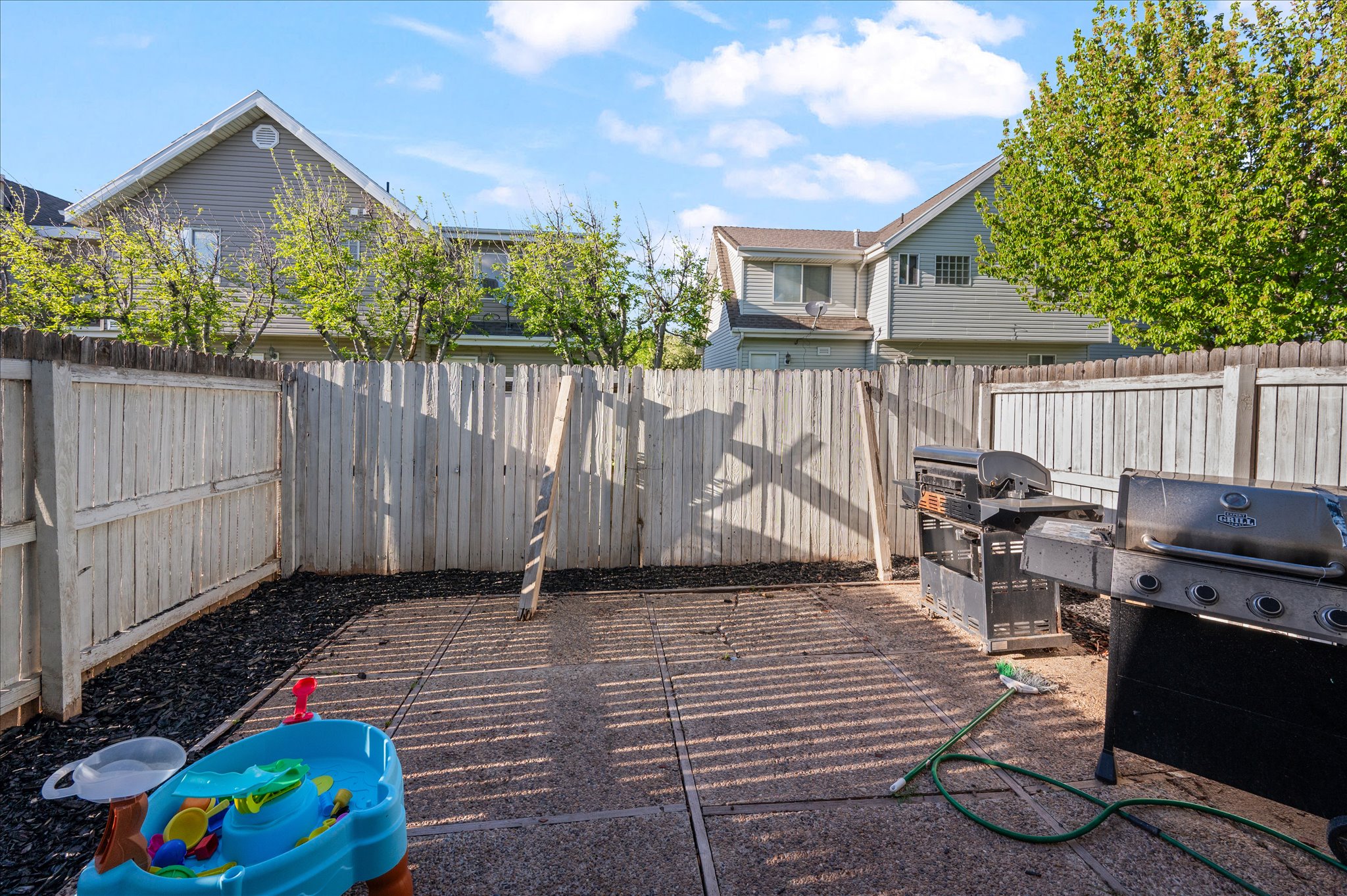 Paved patio area featuring a privacy fence, wood-chip landscaping, and a clear blue sky