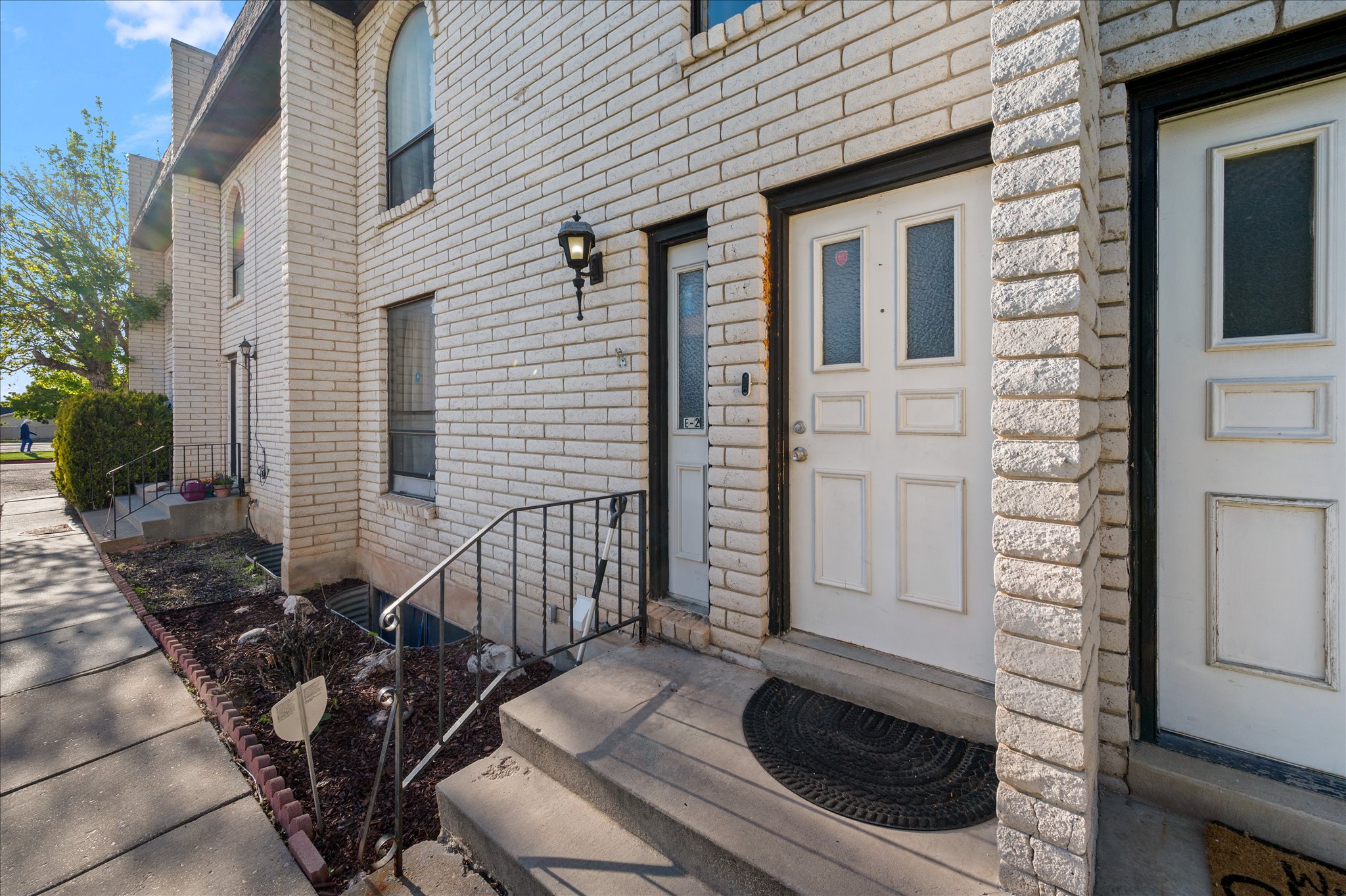 White brick exterior featuring a multi-paneled front door with decorative glass inserts, black wrought iron railing, concrete steps, and a decorative outdoor light fixture