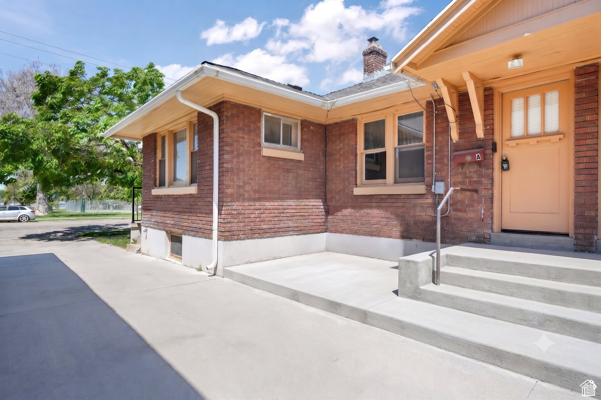 Brick exterior with a prominent entry porch, featuring a wooden door with transom lites, concrete steps, and a metal handrail