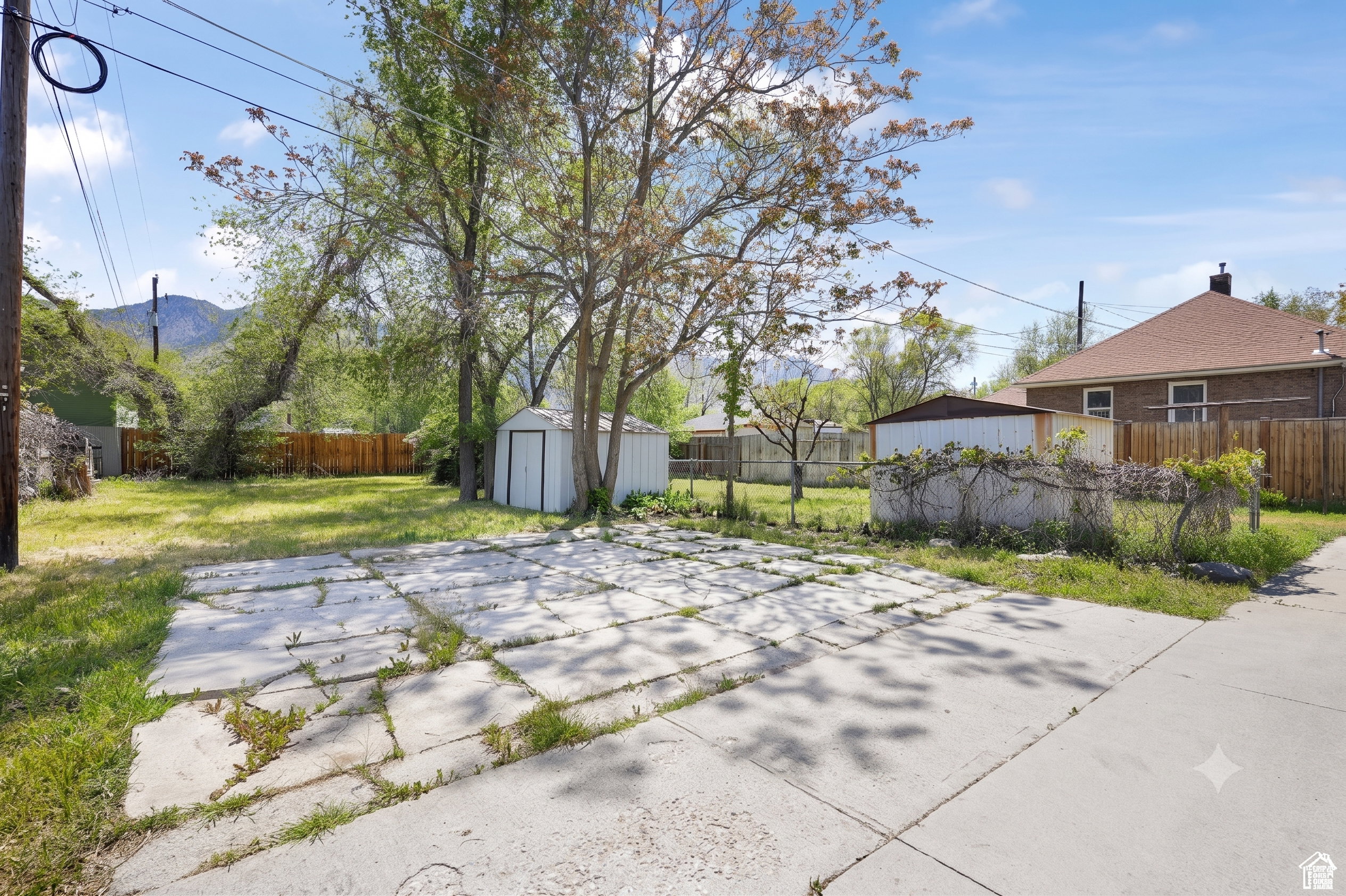 Expansive backyard featuring a concrete patio, mature trees, a storage shed, and partial fencing