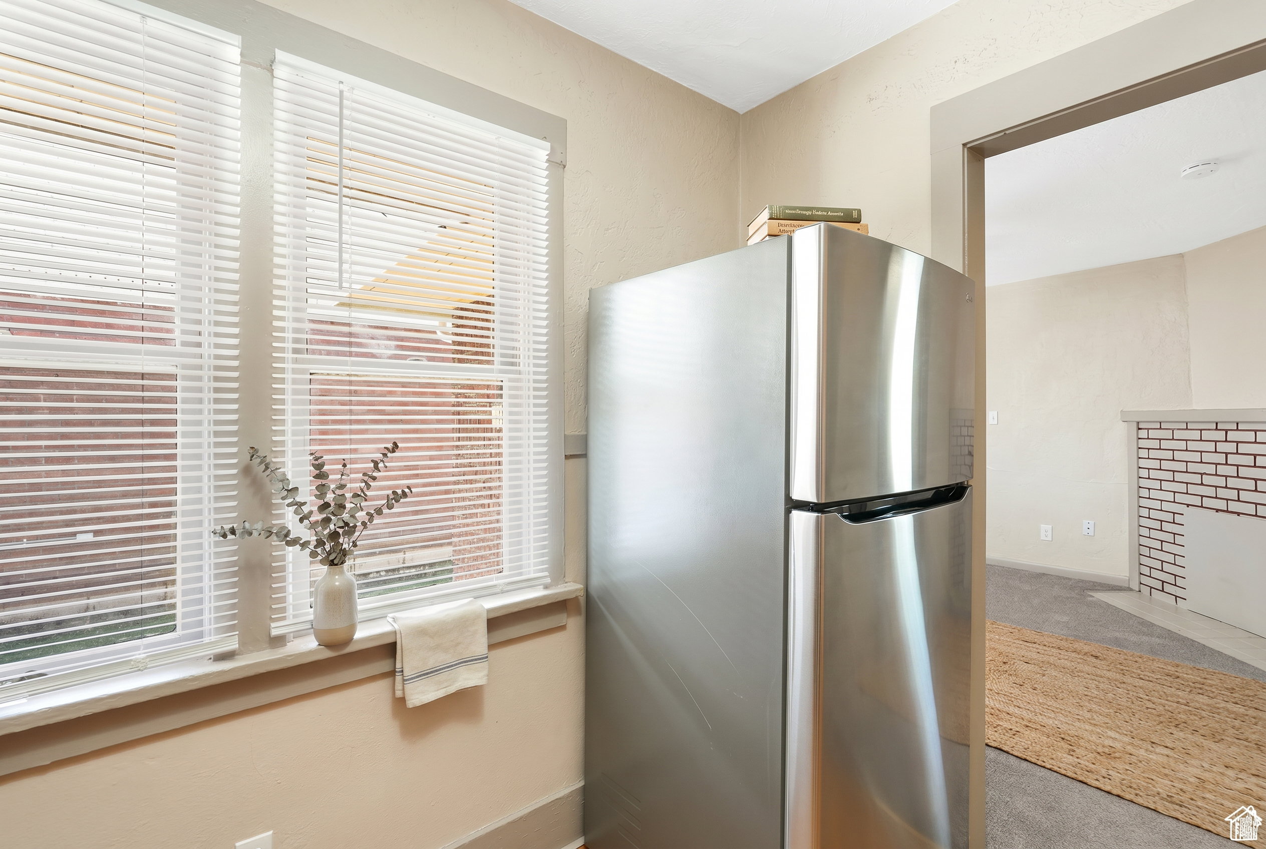 Stainless steel refrigerator with a top freezer, double-hung windows with blinds, and light-toned walls