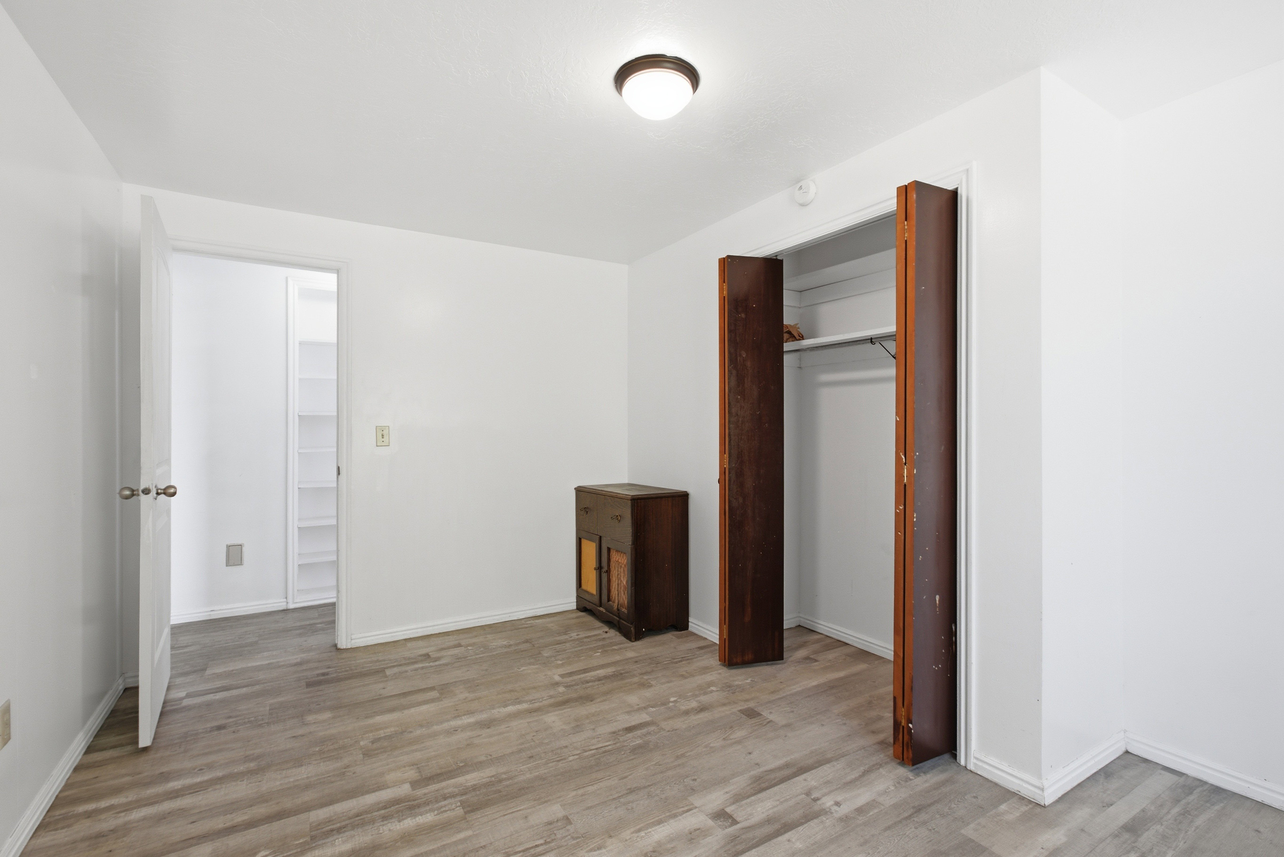 Room featuring wood-finish flooring, white walls, and a recessed closet with bi-fold doors