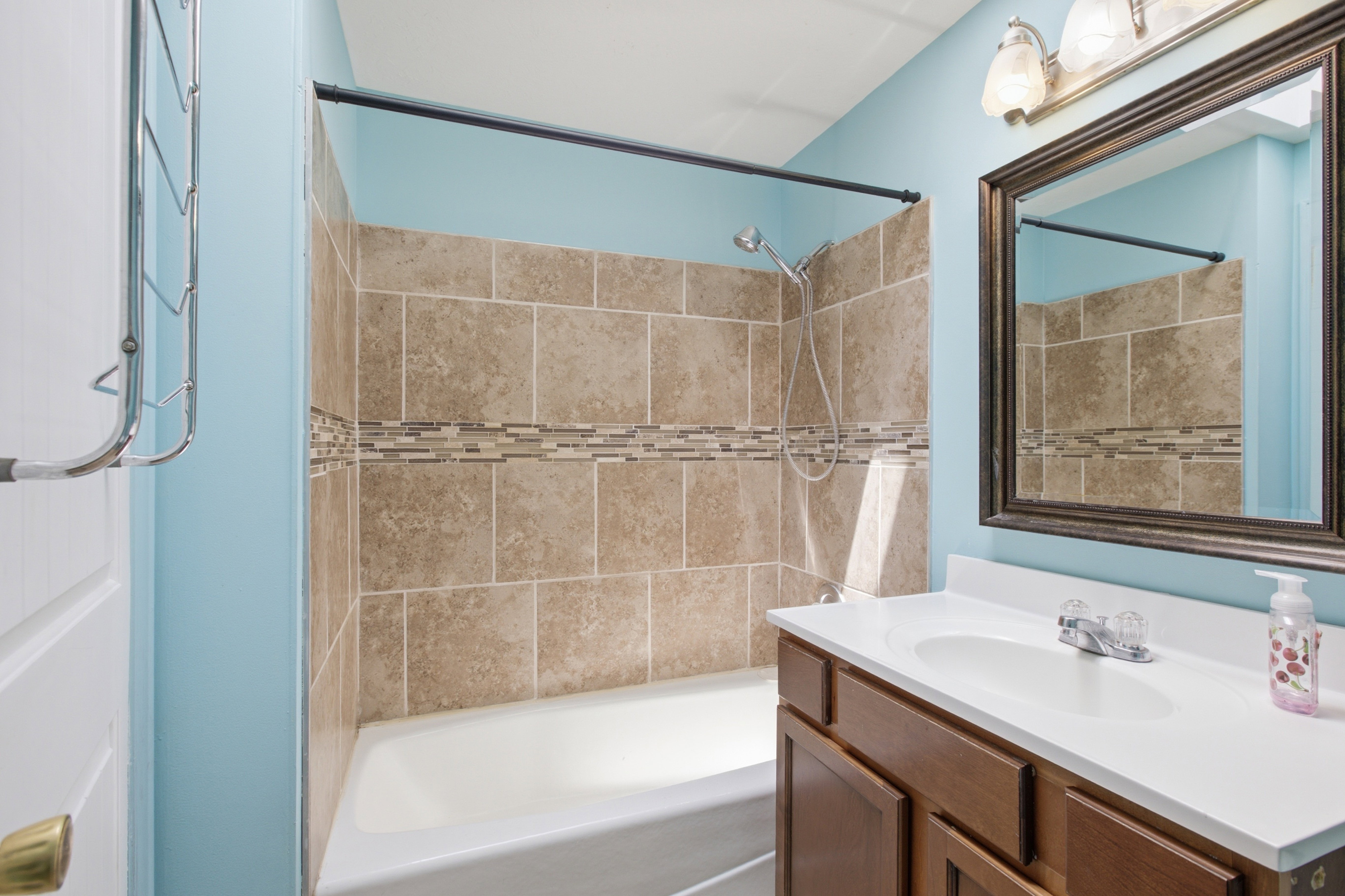 Full bathroom featuring a tub/shower combination with tile surround, decorative mosaic tile accent, and a handheld shower fixture