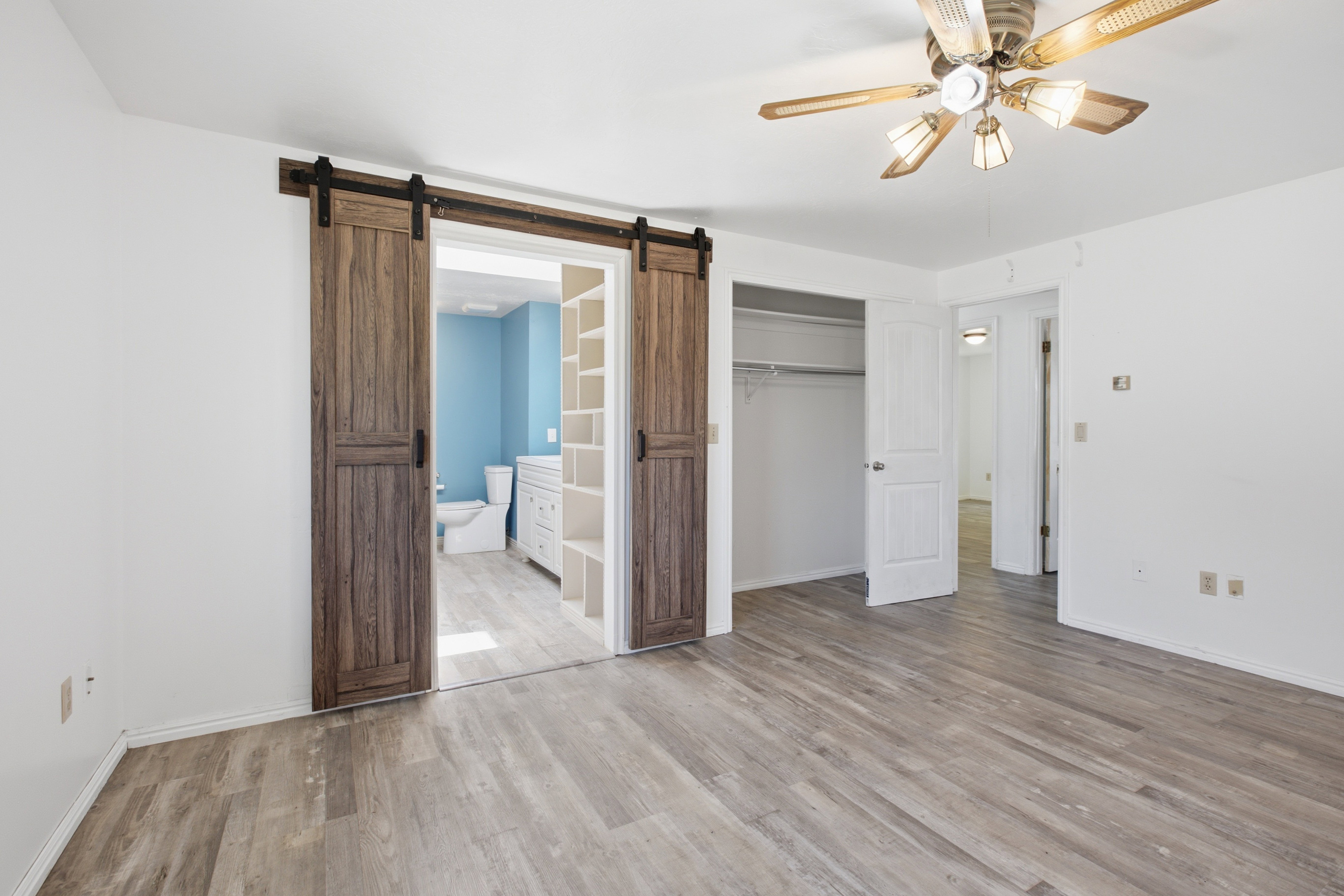 Spacious room featuring wood-finish flooring, a ceiling fan with light fixture, and white painted walls