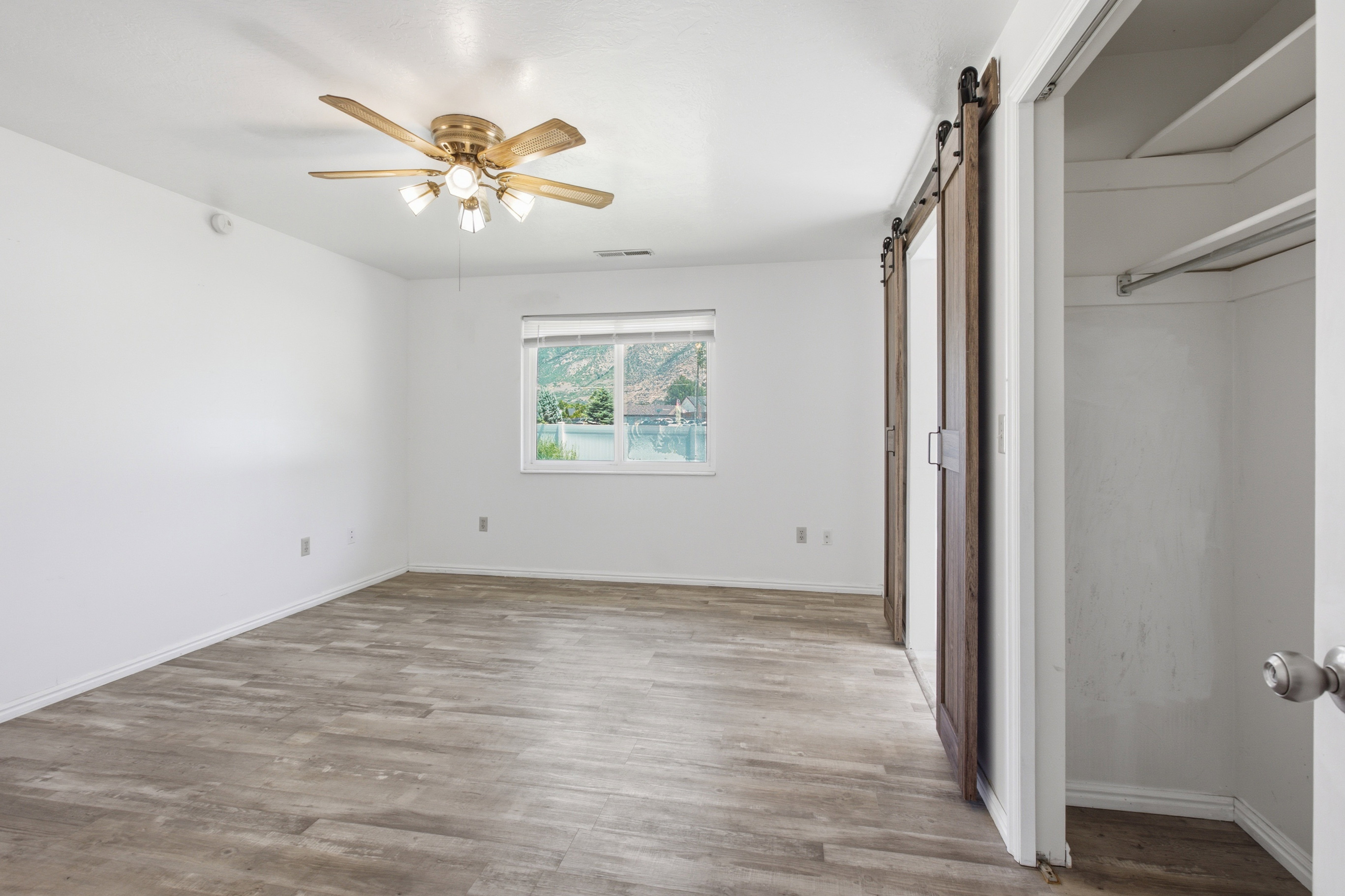 Room featuring wood-finish flooring, white walls, and a ceiling fan with integrated lighting