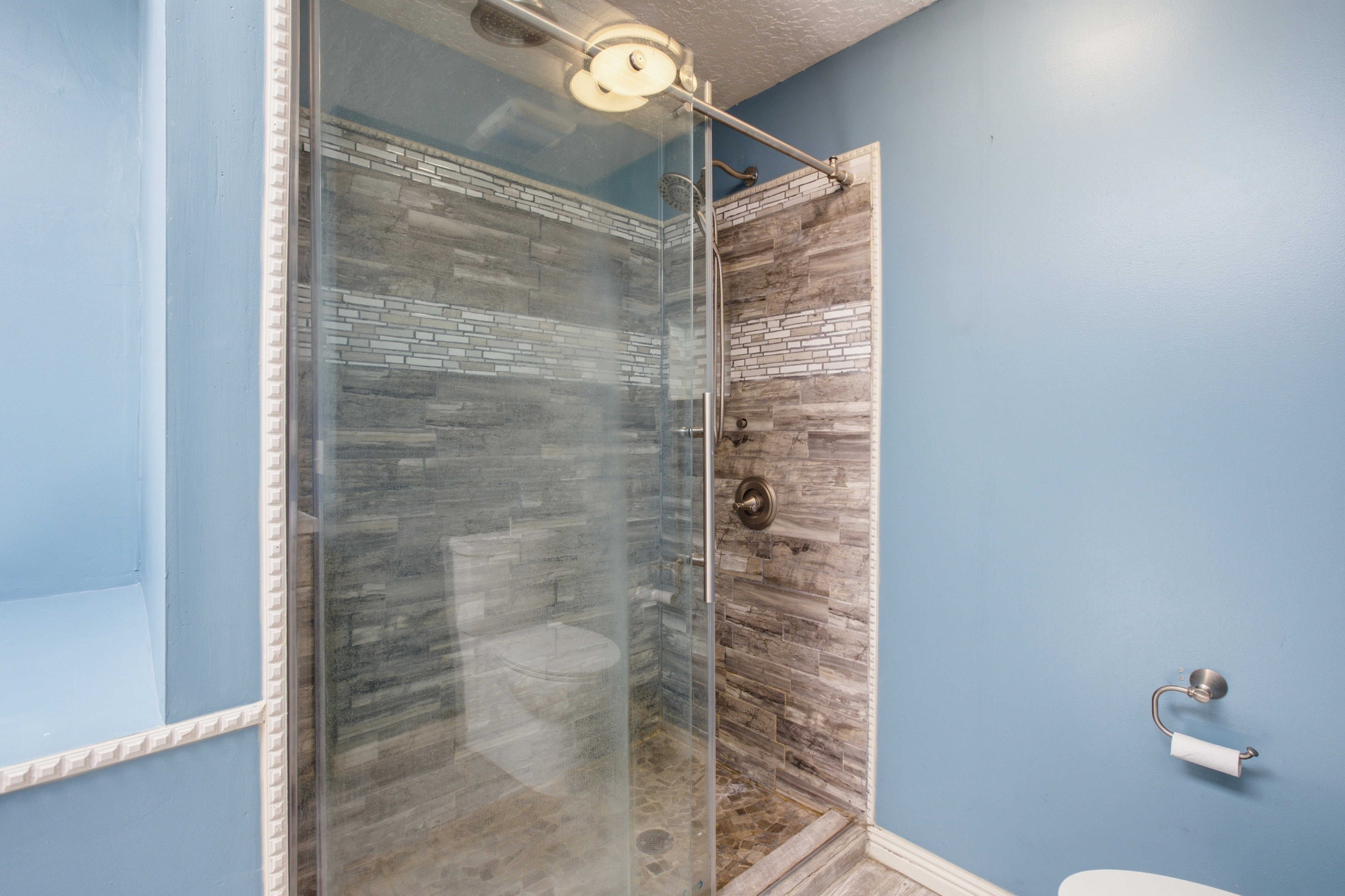 Glass-enclosed shower featuring stacked stone-look tile, a decorative mosaic accent band, and a brushed nickel shower fixture