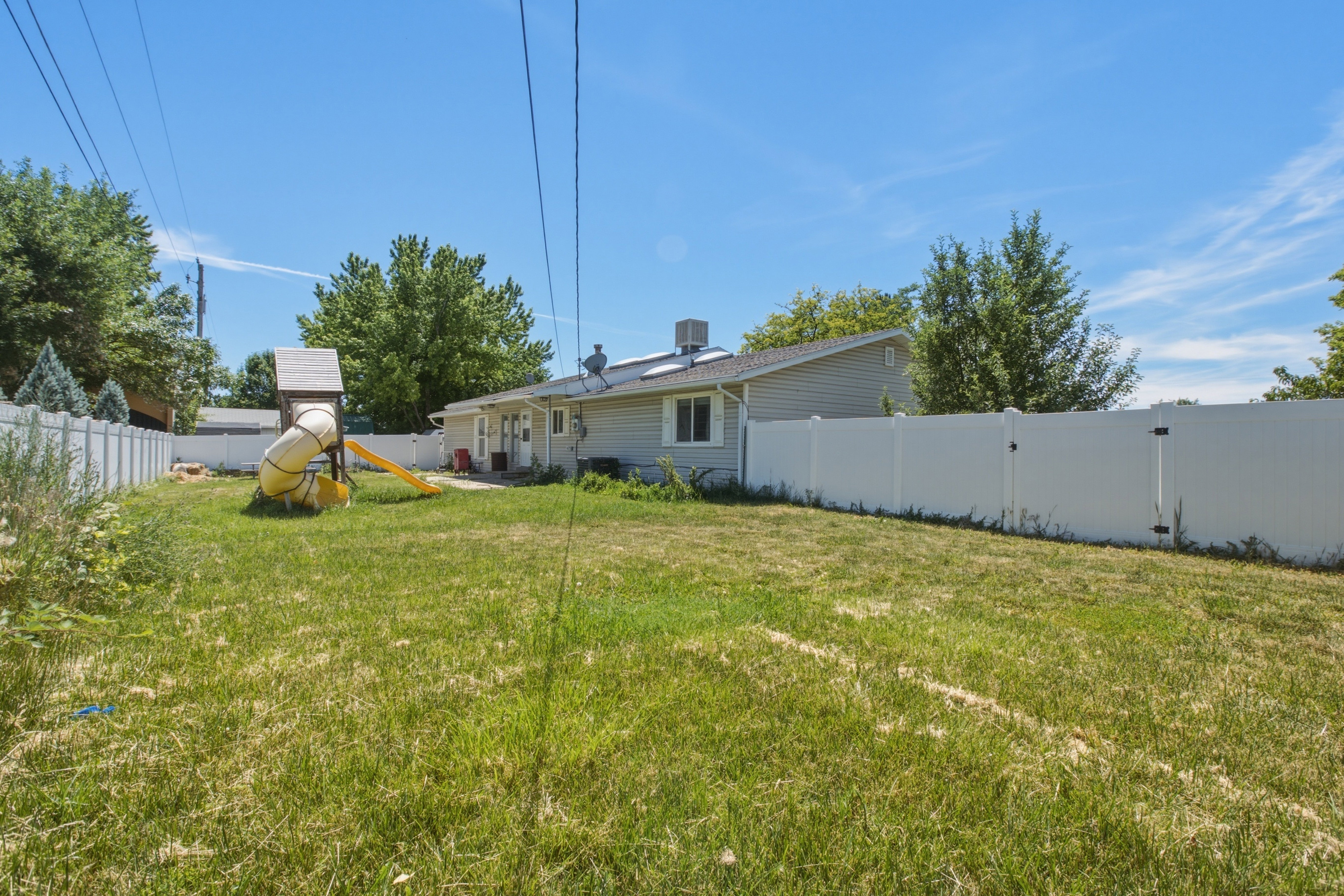 Expansive backyard featuring a partial white vinyl privacy fence, a detached residential structure with light-colored siding, and a visible back entrance