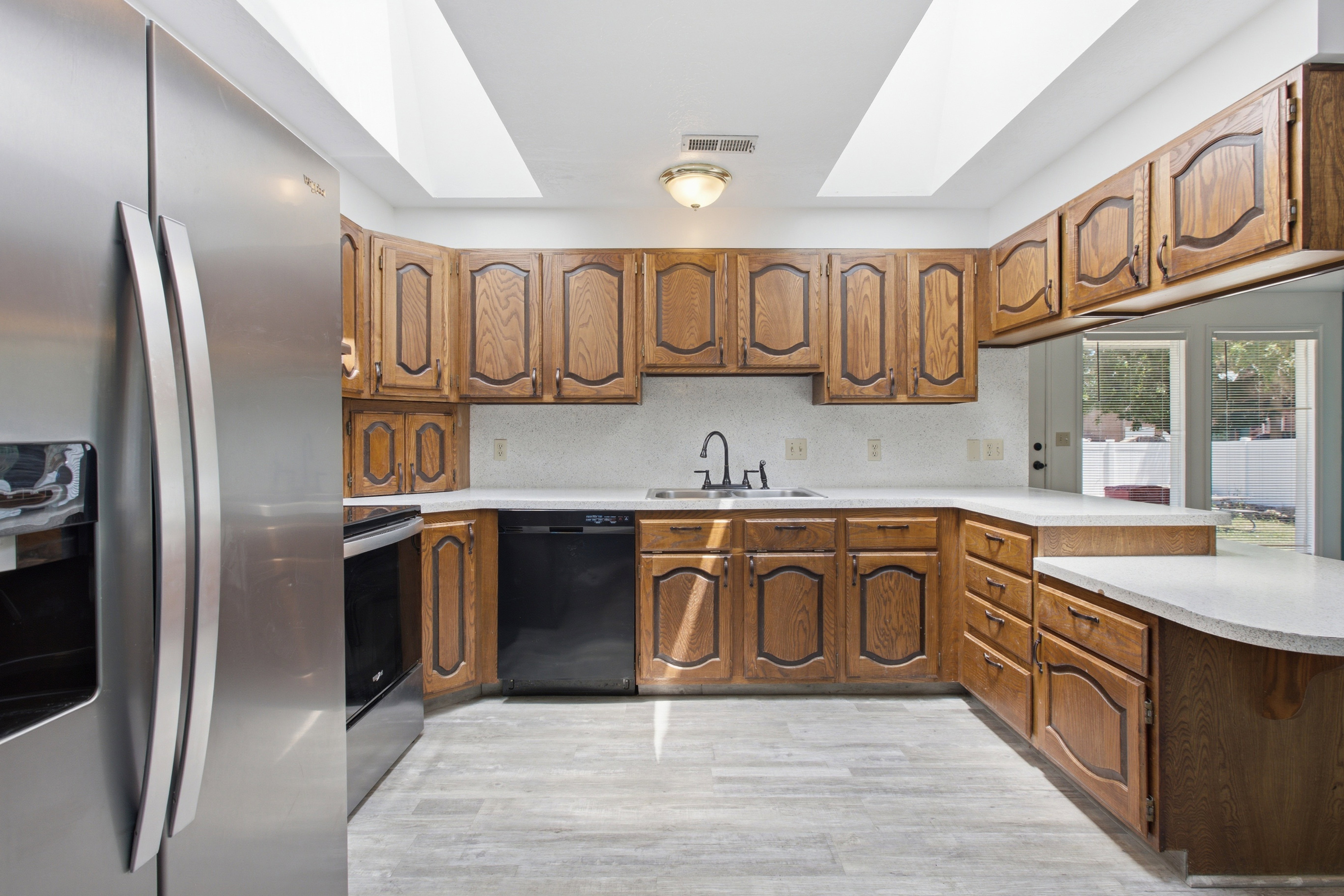 Kitchen featuring wood-finish cabinetry, light countertops, wood-finish flooring, and a stainless steel refrigerator