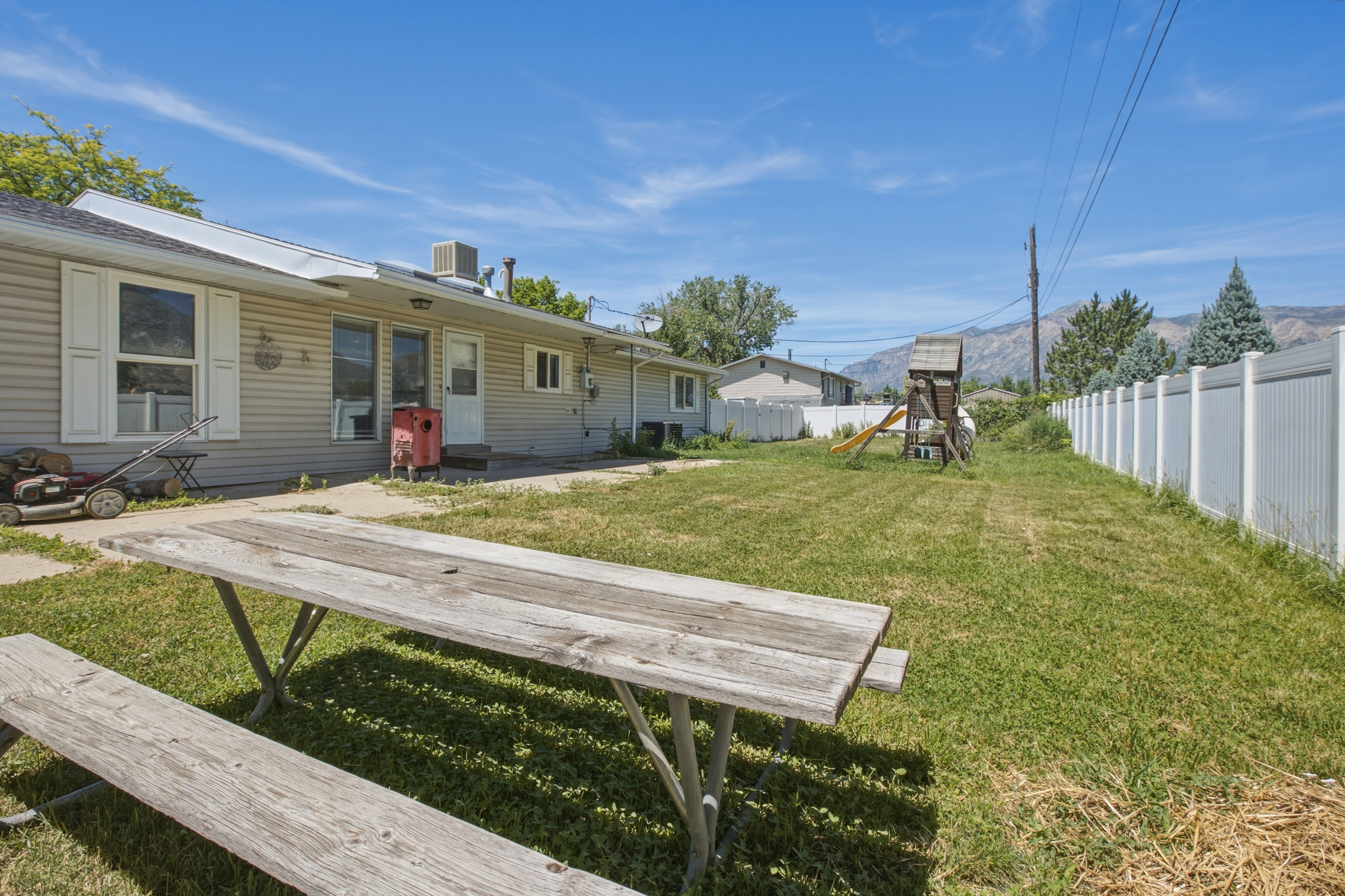 Expansive backyard with a manicured lawn, white privacy fencing, and a concrete patio