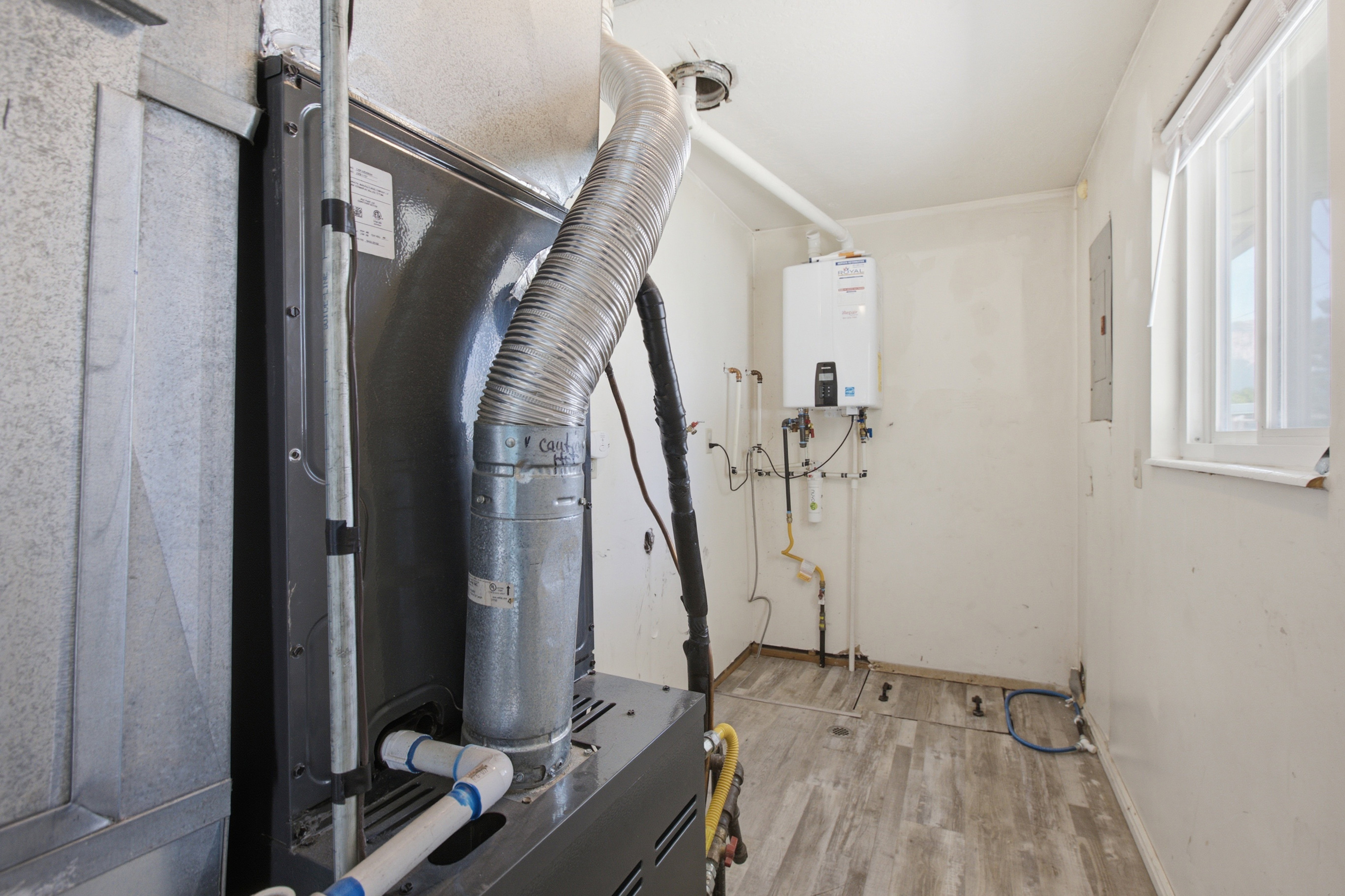 Utility room featuring a wall-mounted tankless water heater, a central air conditioning unit, wood-finish flooring, and a single window with white blinds