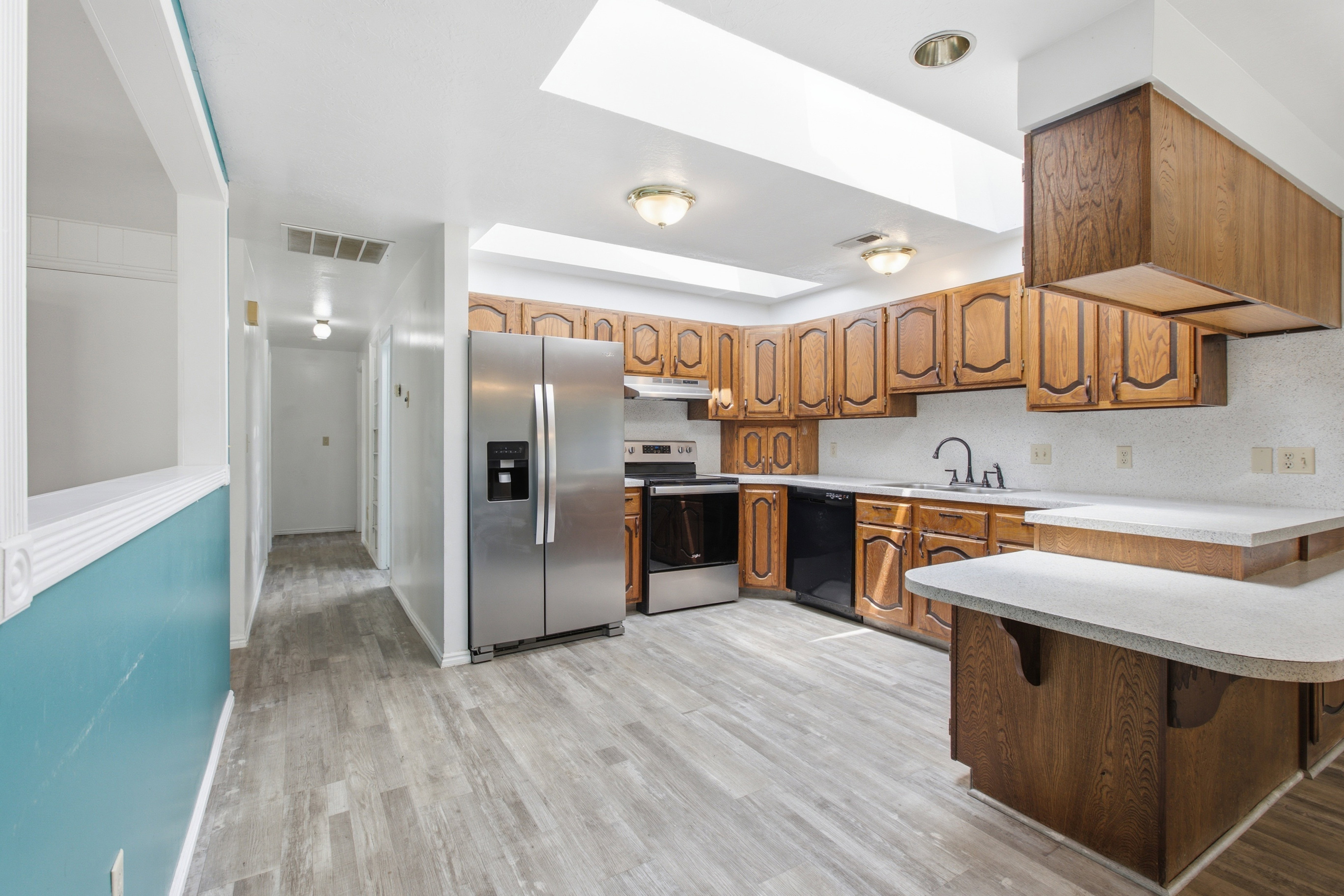 Kitchen featuring wood-finish cabinetry, light-toned countertops, and a full suite of stainless steel and black appliances