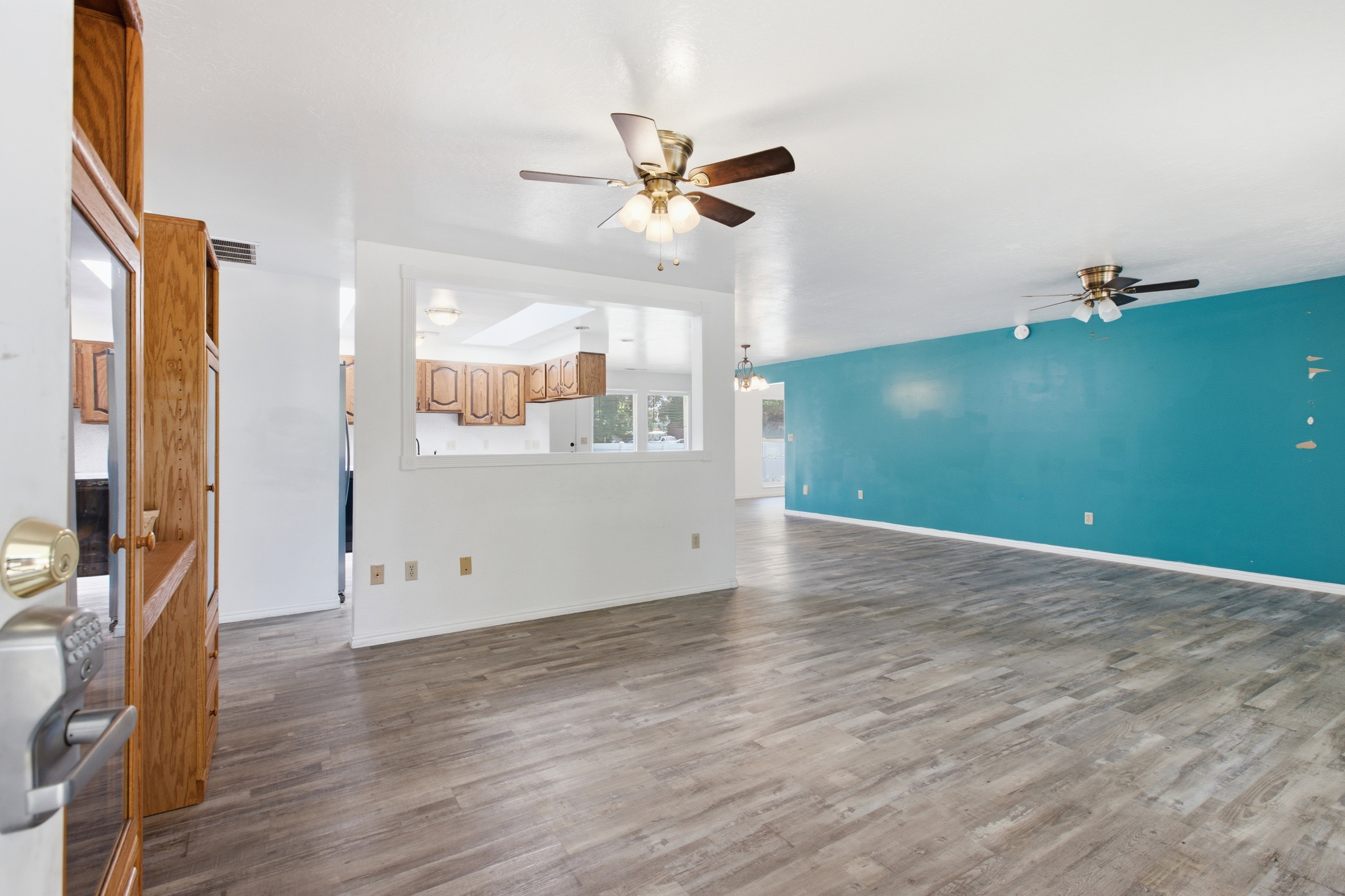 Spacious interior featuring wood-finish flooring, a vibrant accent wall, and multiple ceiling fans