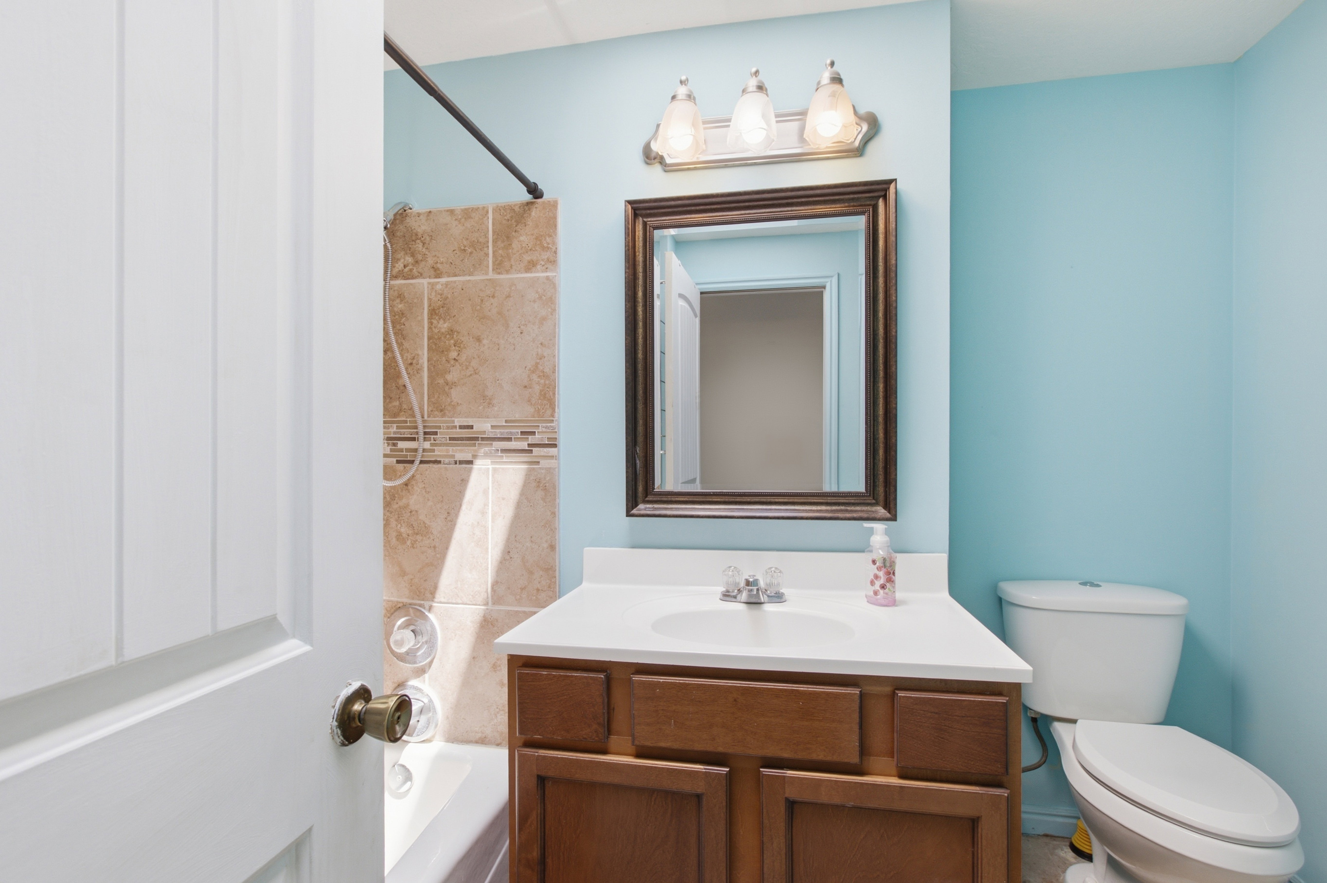 Bathroom featuring a single vanity with a white countertop, a bronze-framed mirror, and a three-light fixture