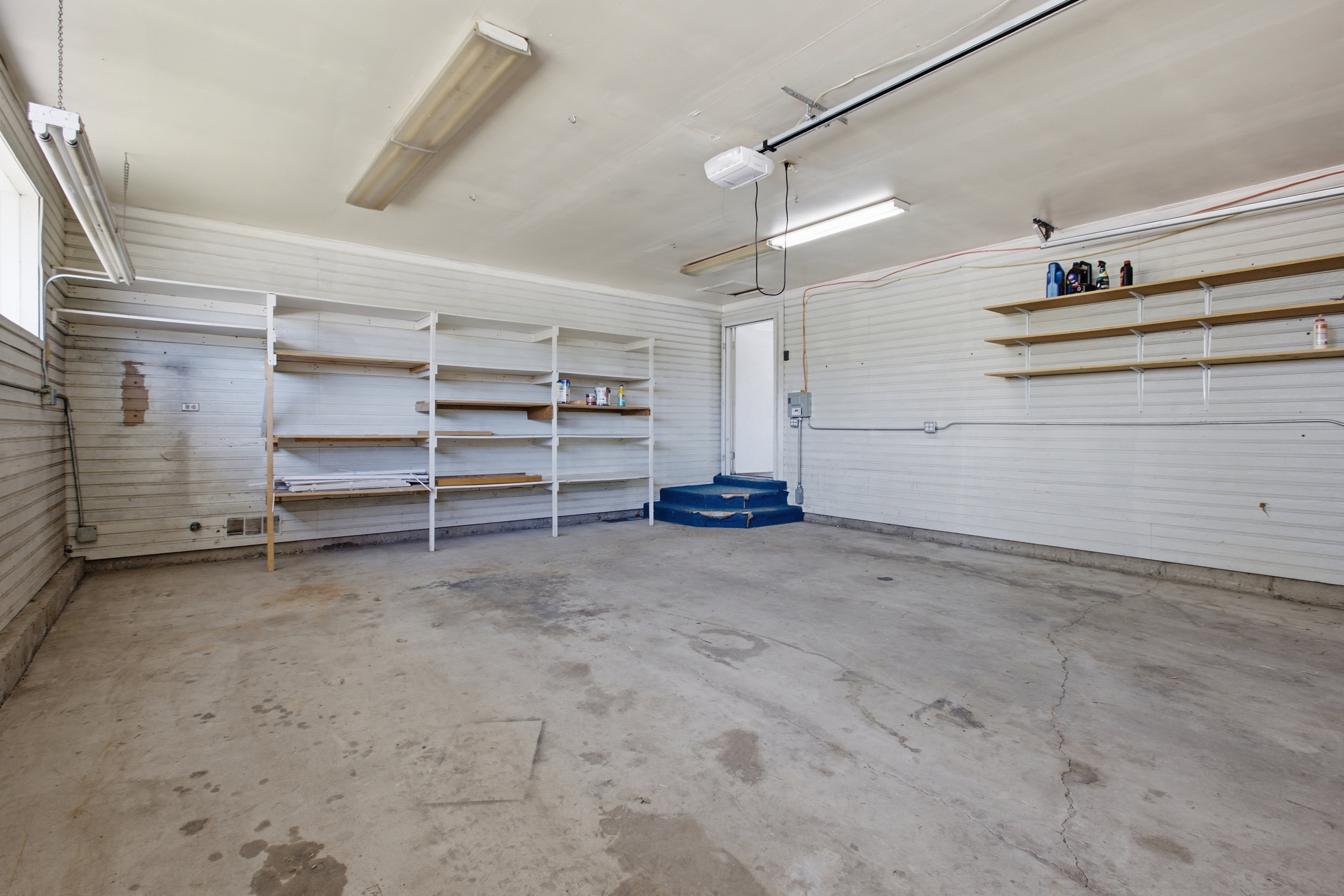Spacious garage with concrete flooring, fluorescent overhead lighting, and built-in shelving units
