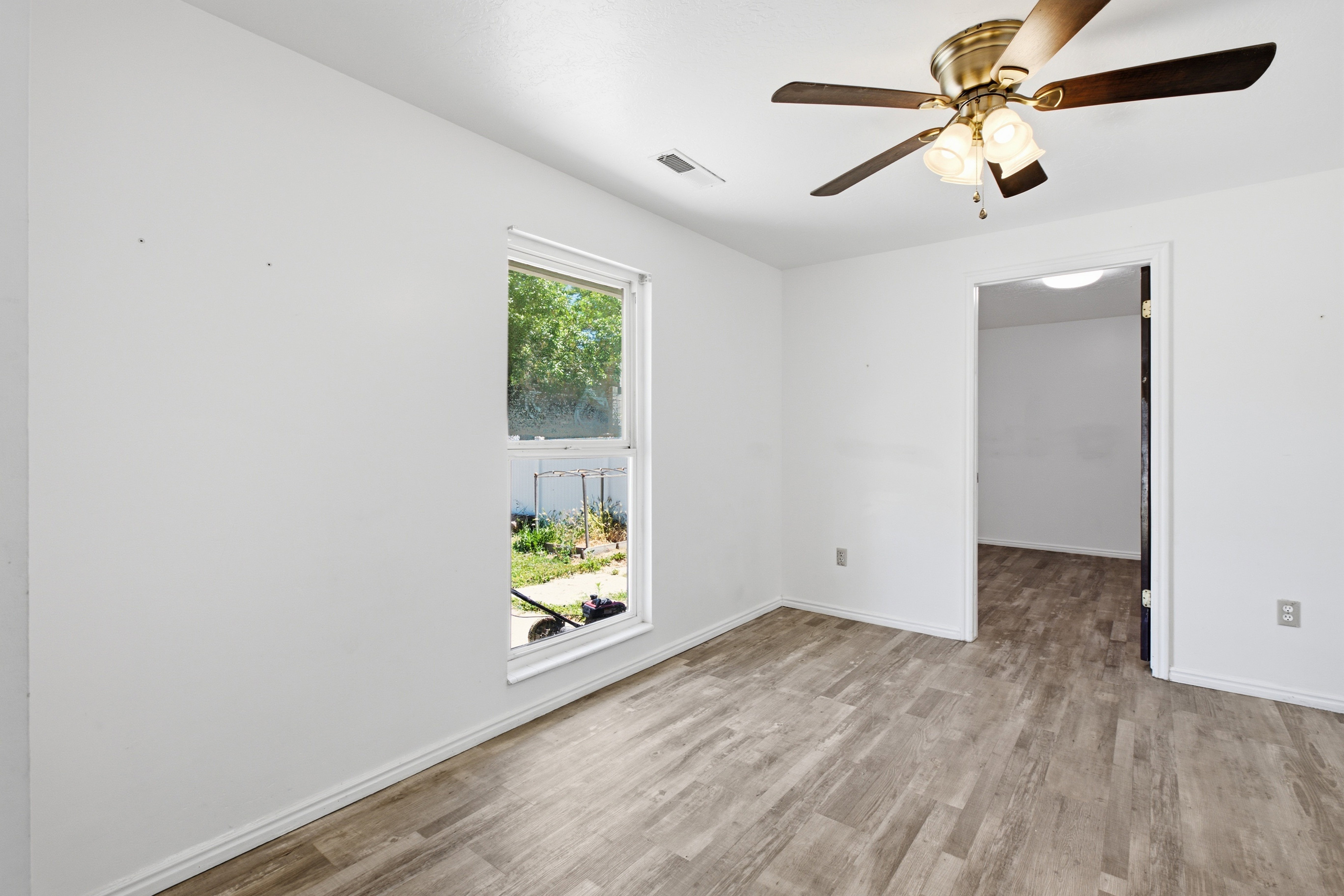 Spacious room featuring wood-finish flooring and a ceiling fan with integrated lighting