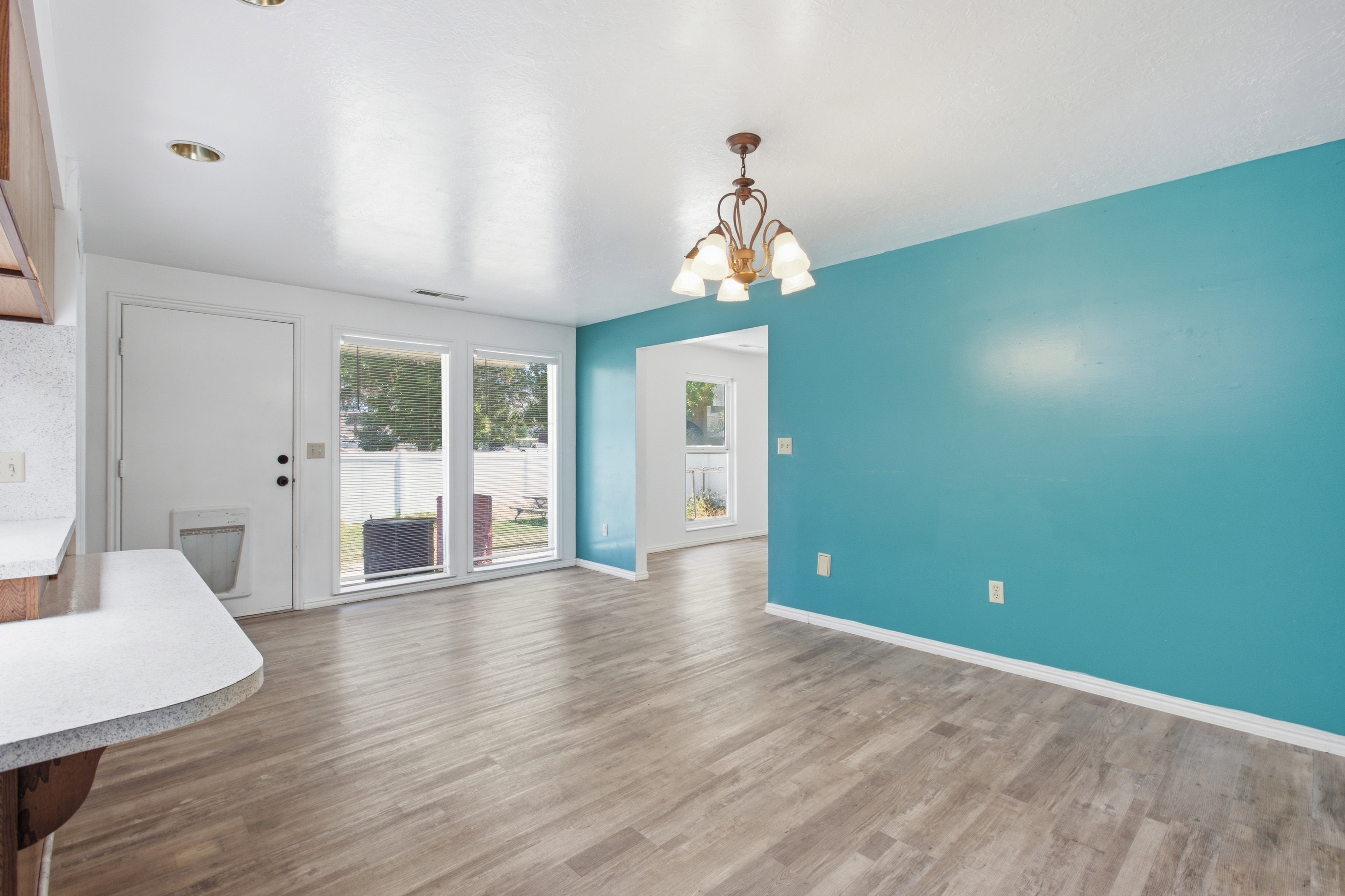 Spacious interior room featuring wood-finish flooring, a vibrant accent wall, and a multi-light chandelier