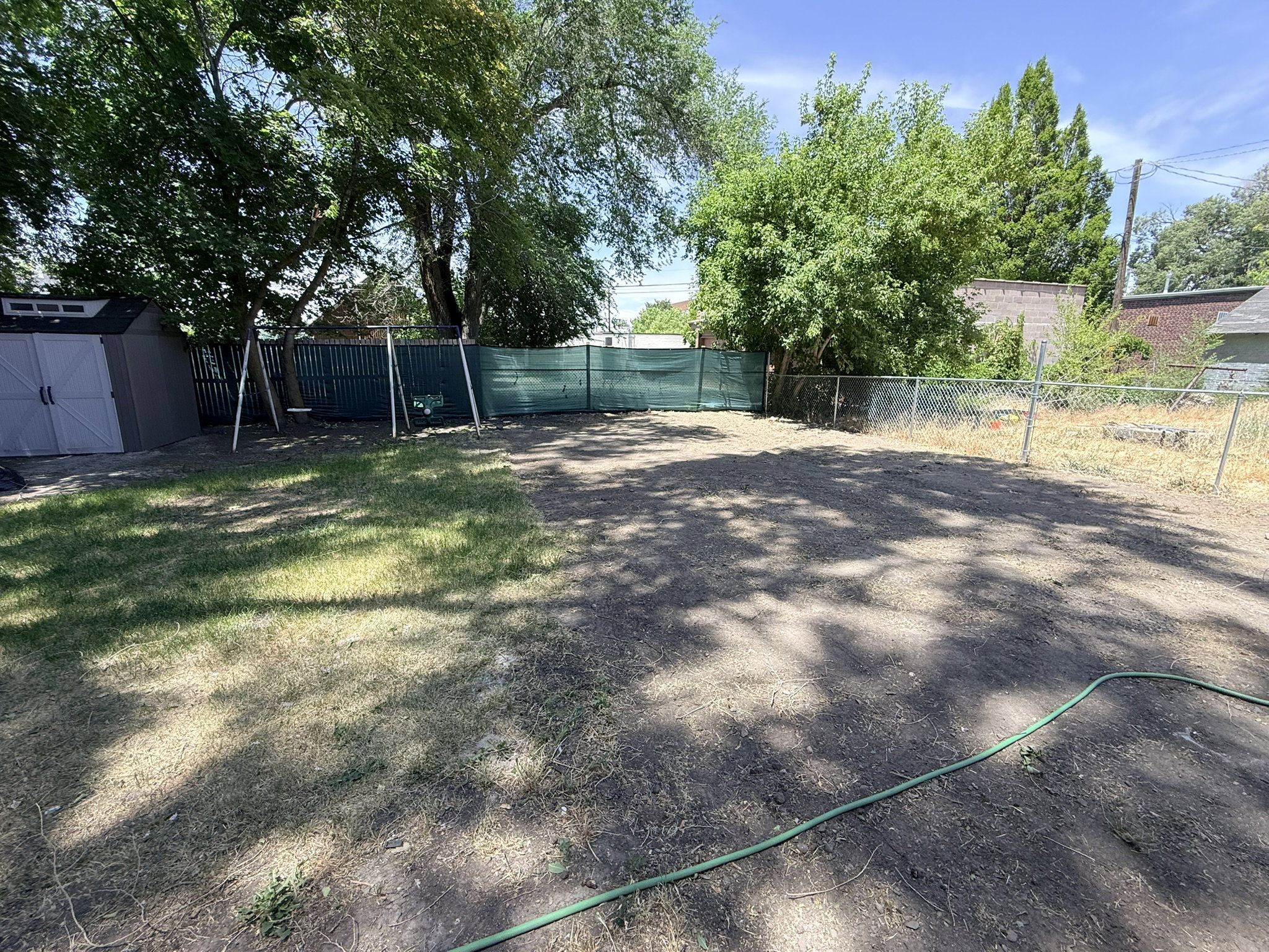 Expansive outdoor space featuring a storage shed, chain-link fencing, mature trees, and a swing set