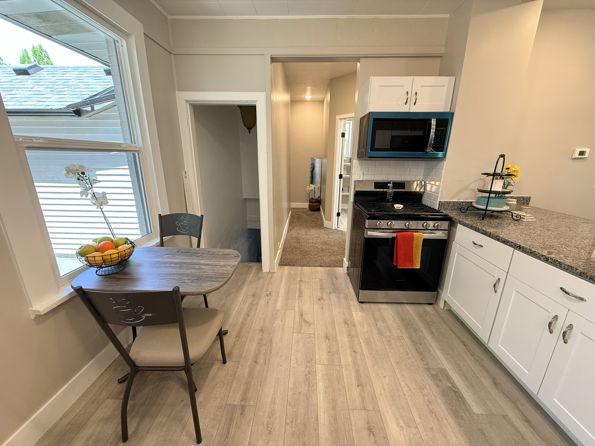 Compact kitchen featuring white shaker cabinetry, granite-finish countertops, stainless steel range, and a built-in microwave