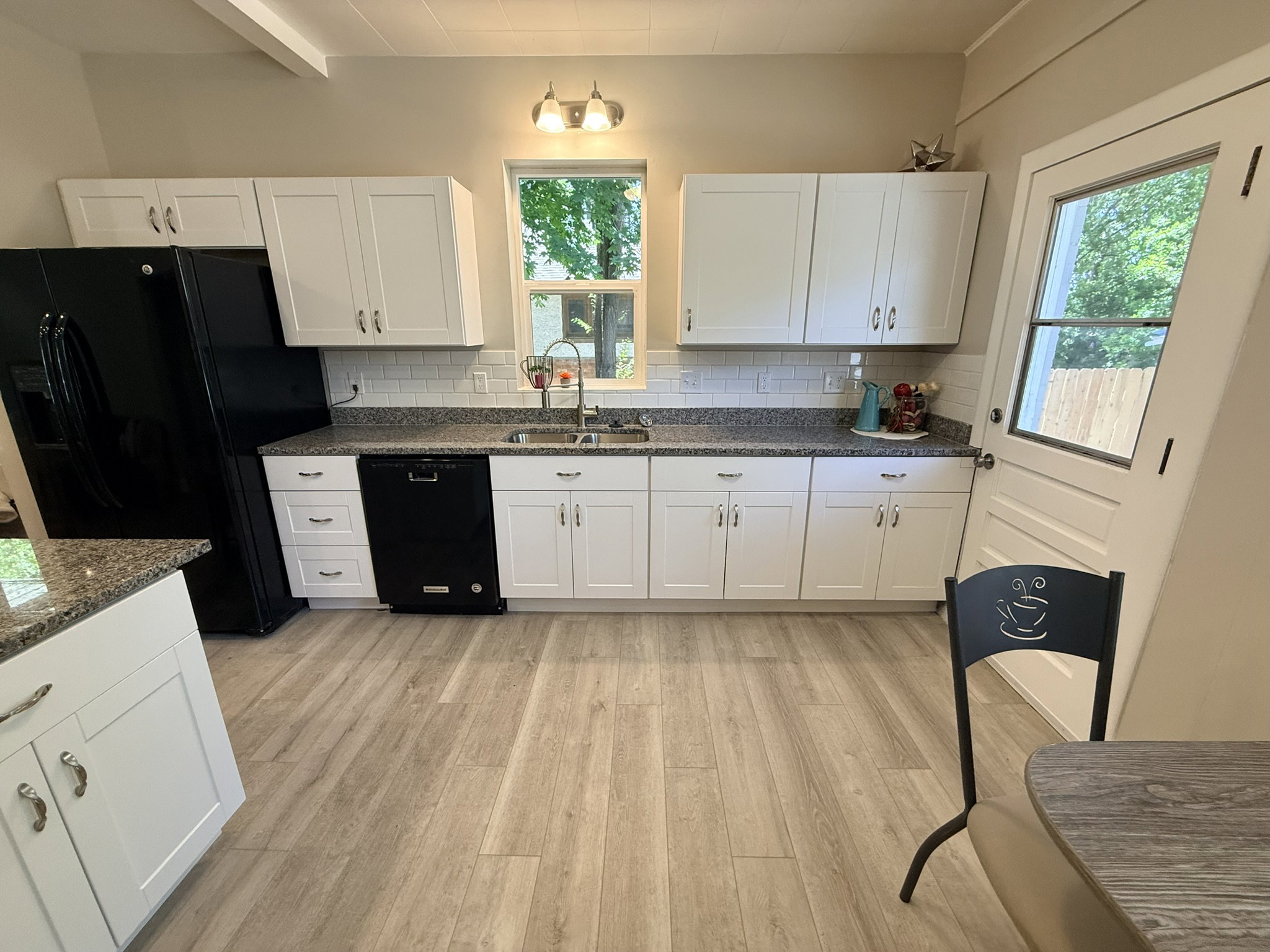 Kitchen featuring white shaker-style cabinetry, dark speckled countertops, a white subway tile backsplash, and wood-finish flooring